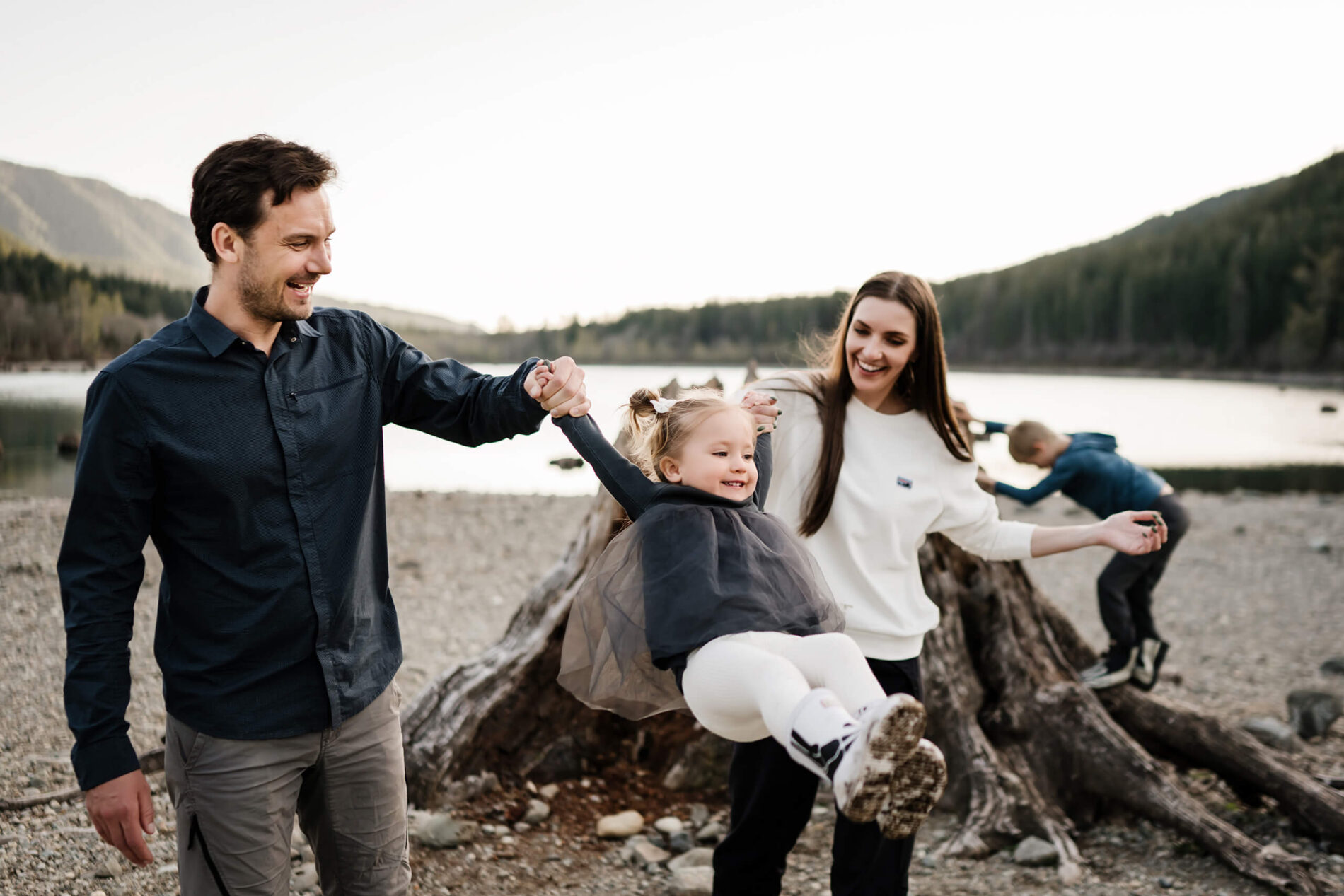 A lifestyle family photo session of mom and dad playing with their daughter while their son is climbing a tree trunk
