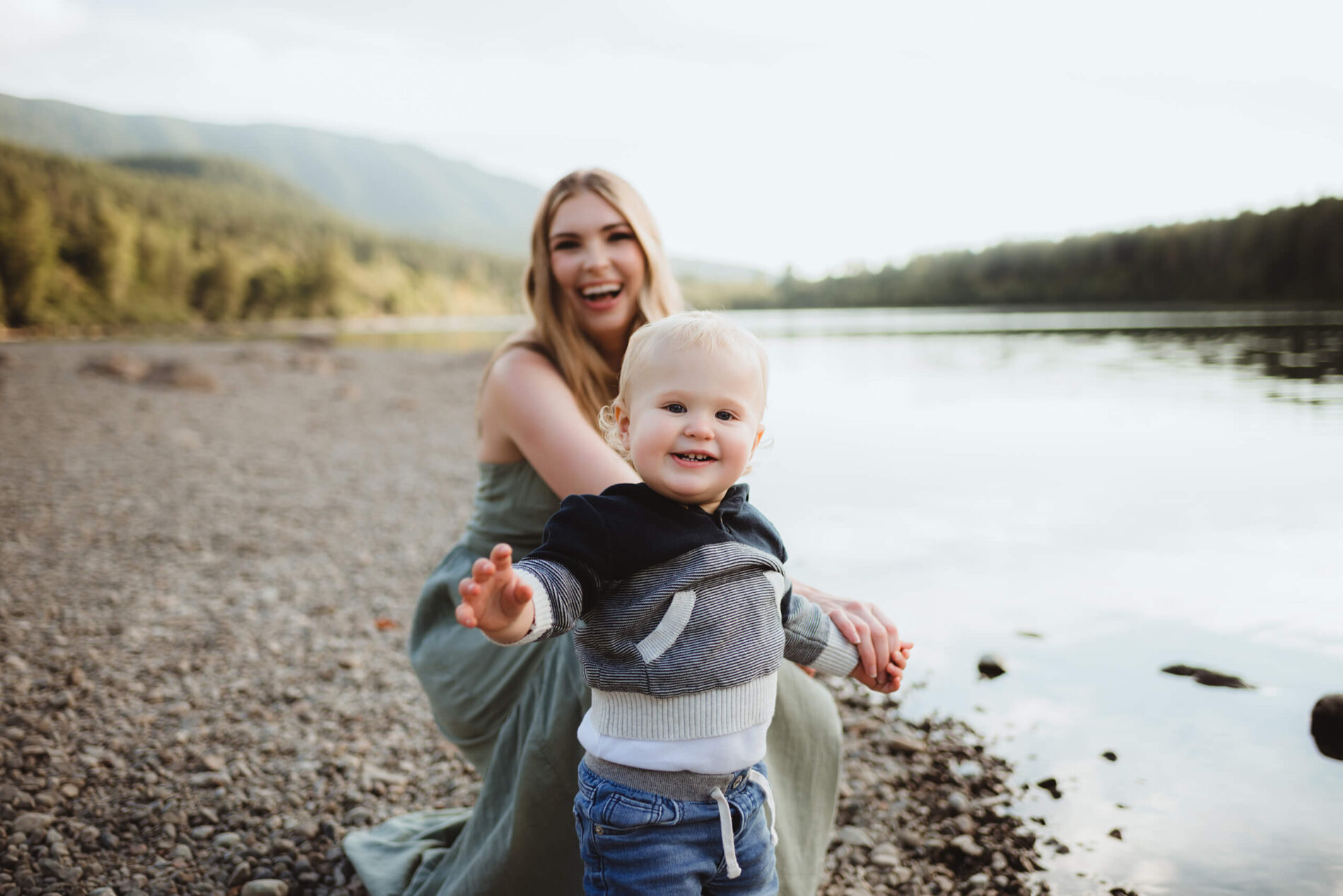 Smiling mom and son playing on the beach of a lake with mountain views in the background