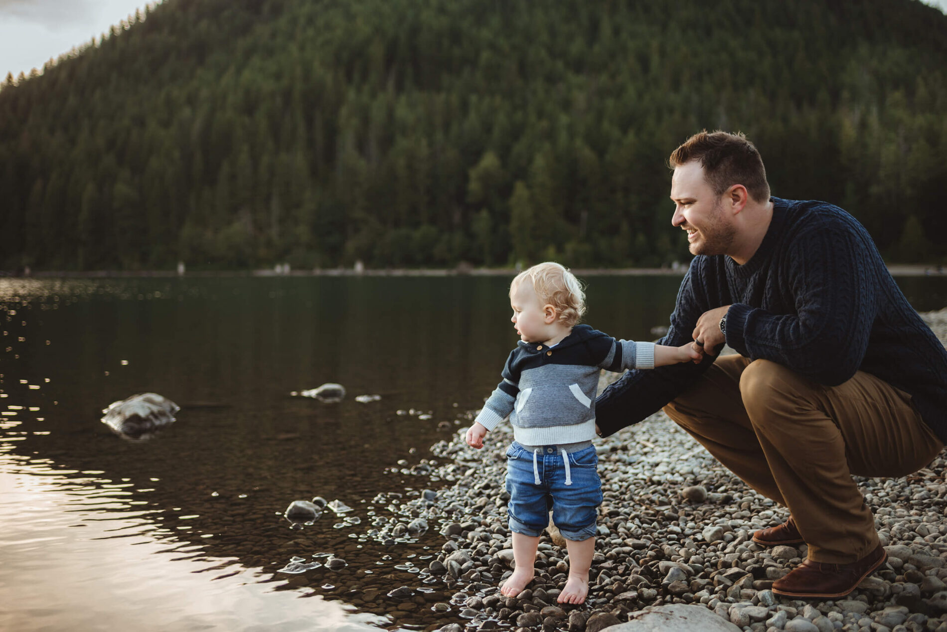 Family portrait of a happy dad with his toddler son at a lake with beautiful mountains in the background