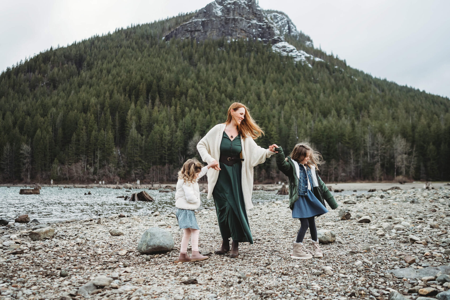 A moment during family photo session of mom holding the hands of her two daughters with mountain in the background