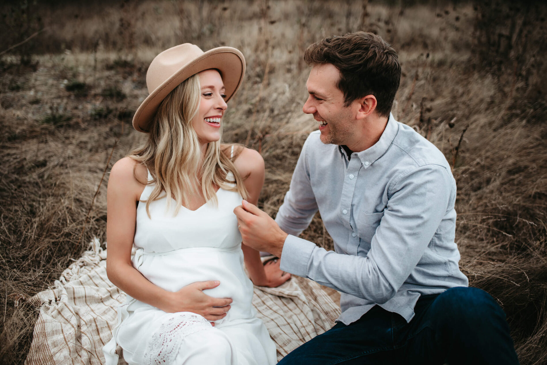 Outdoor maternity photoshoot in the Seattle area of husband and wife sitting in a field, talking and laughing
