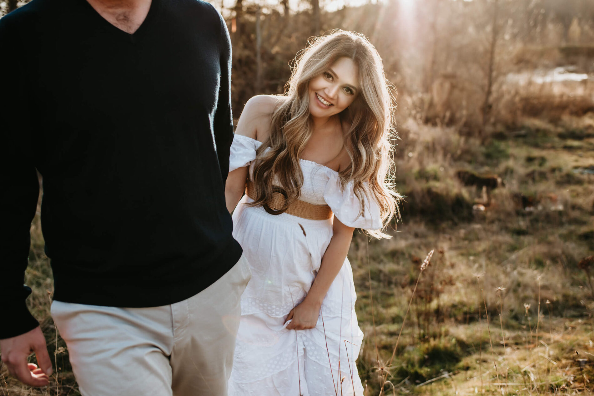 Couples maternity photoshoot pose with husband leading his wife through a field