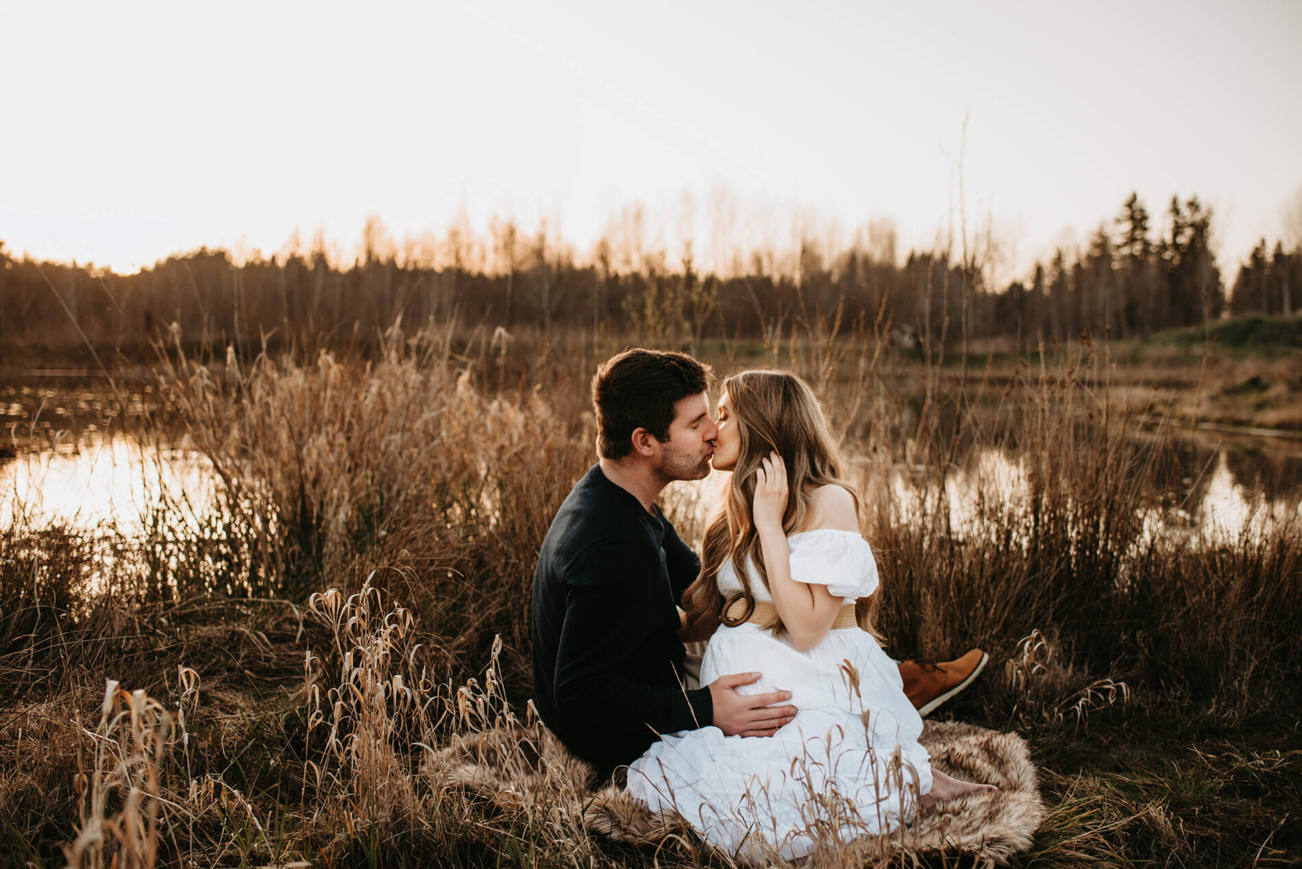 A moment from maternity photoshoot of a couple kissing with the husband holding his hand on wife's belly