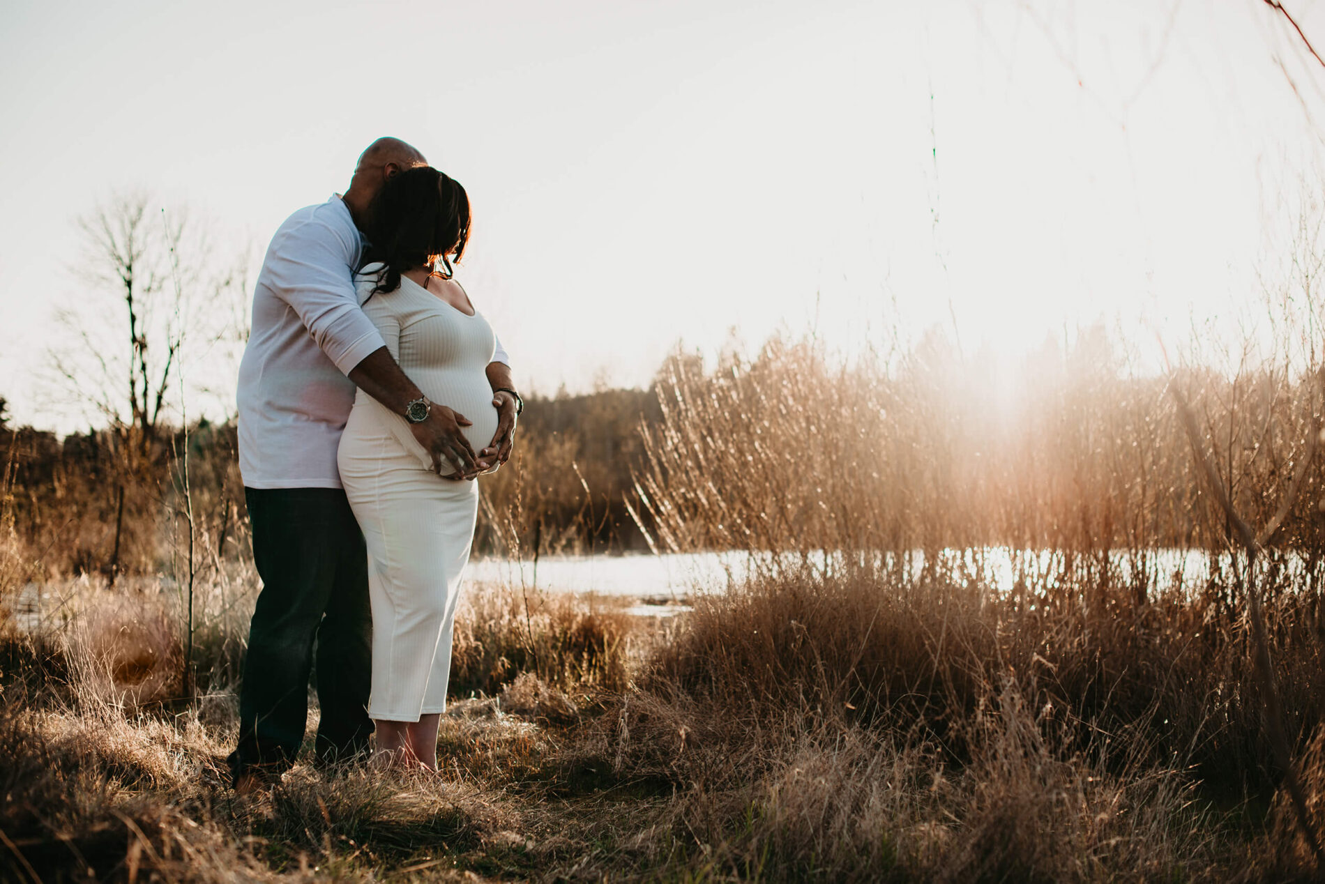 A couple maternity photoshoot in the Seattle area with a husband lovingly hugging his wife from behind with his arms on her belly