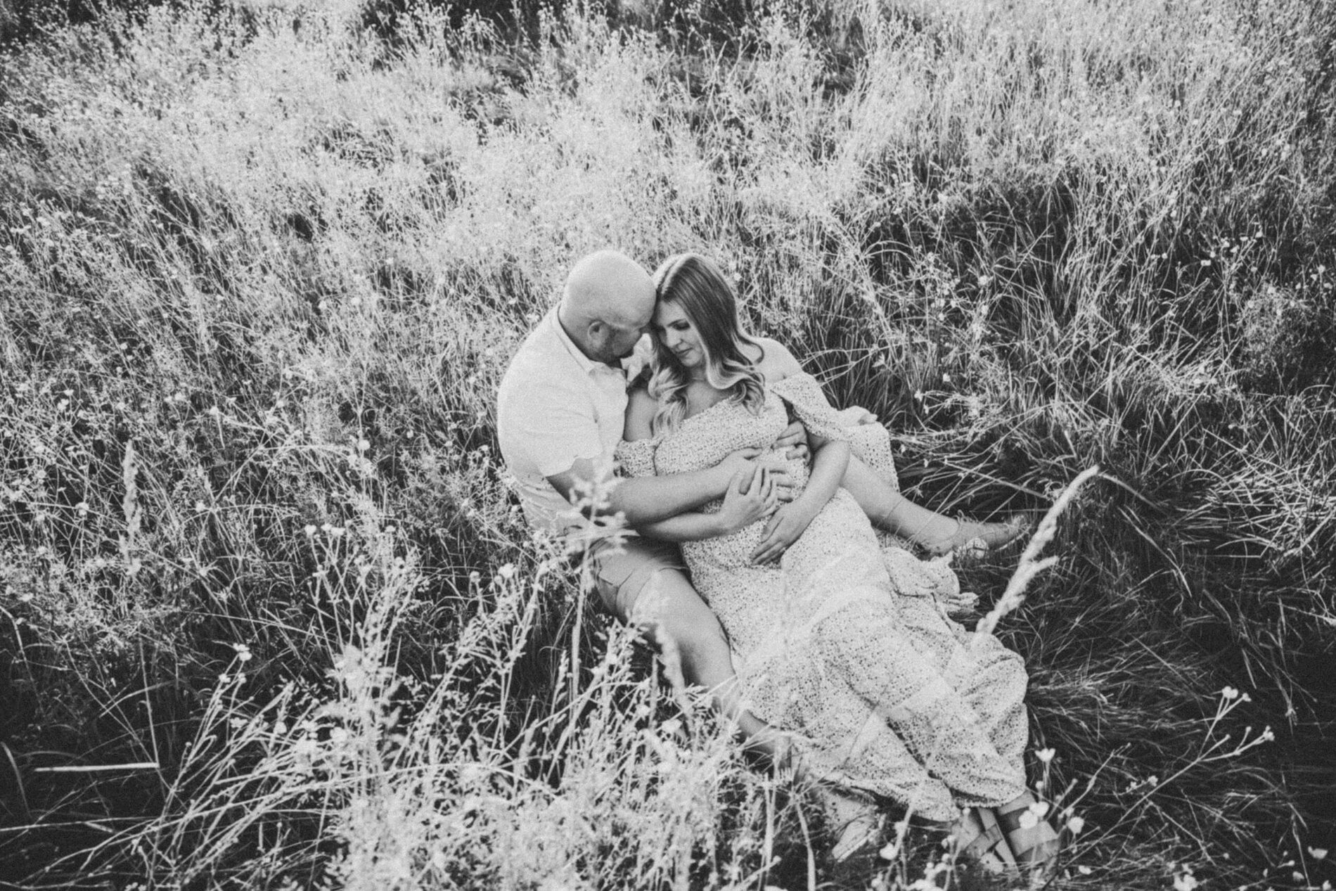 Black and white couples maternity photo of husband lovingly hugging his wife, with their heads touching