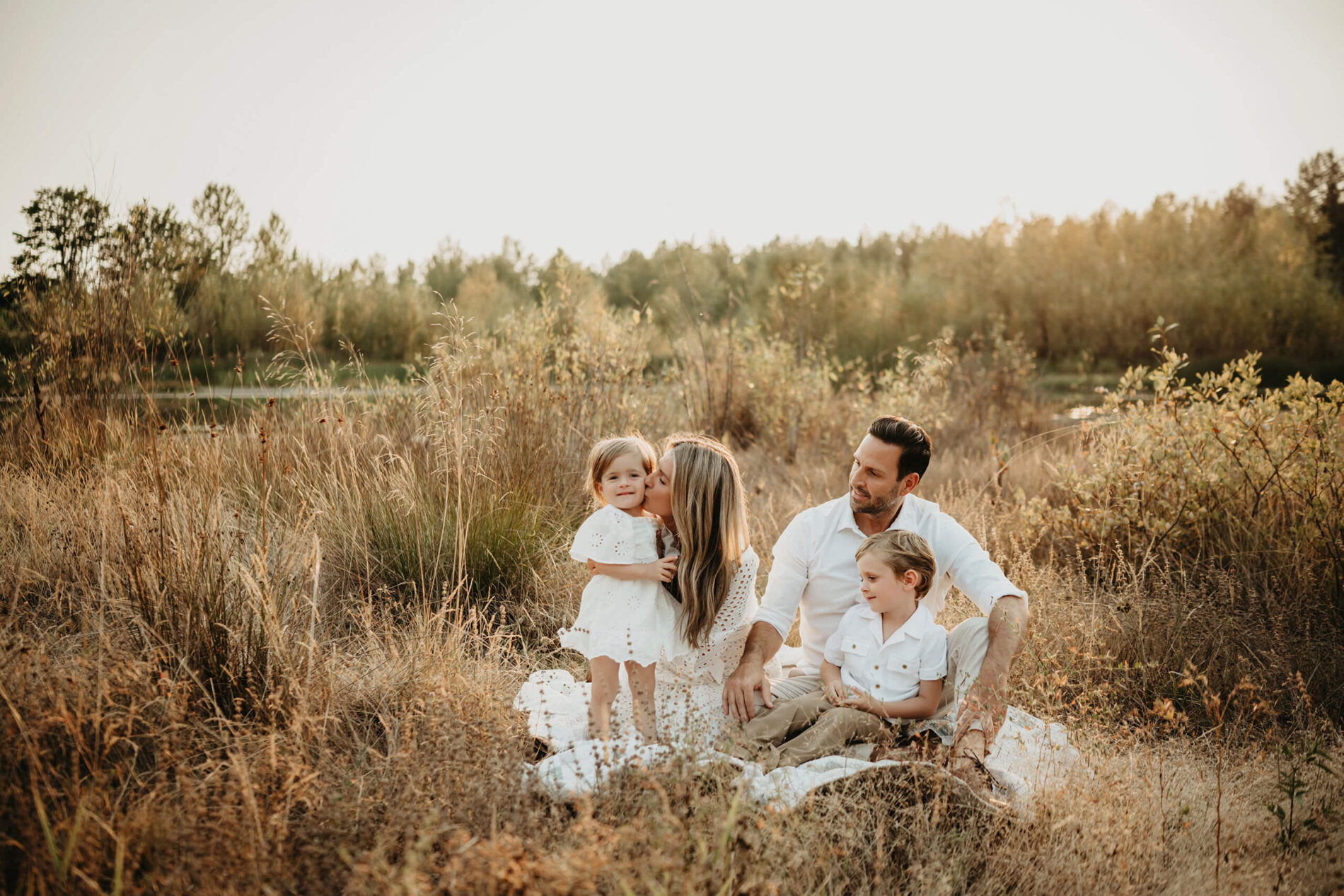 Family photo shoot in Redmond, WA - mom in white dress sitting with her husband, son, and daughter in a beautiful field