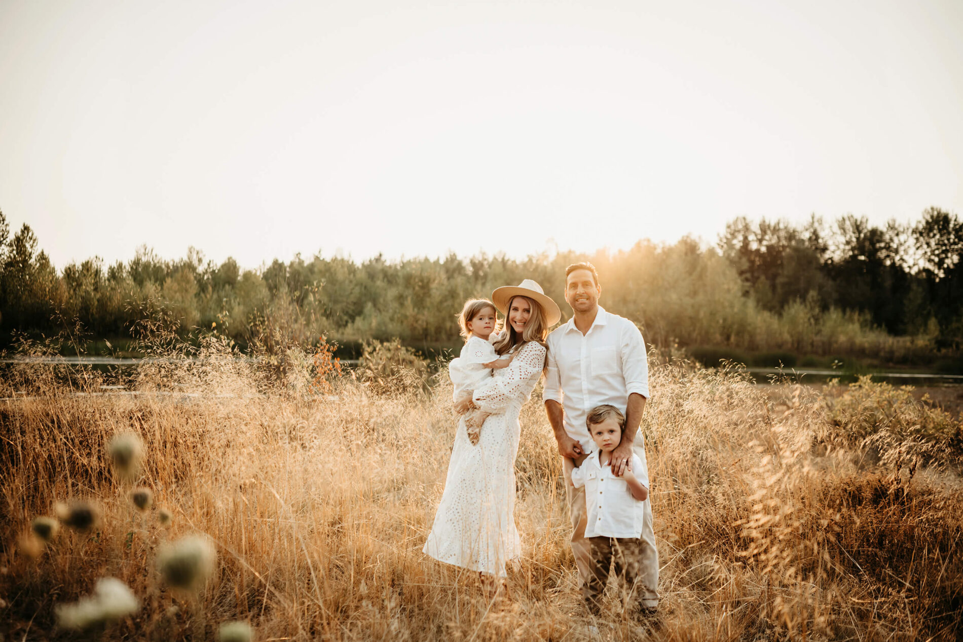 Family photo shoot in Redmond, WA - mom in white dress posing with her husband, son, and daughter in a beautiful field