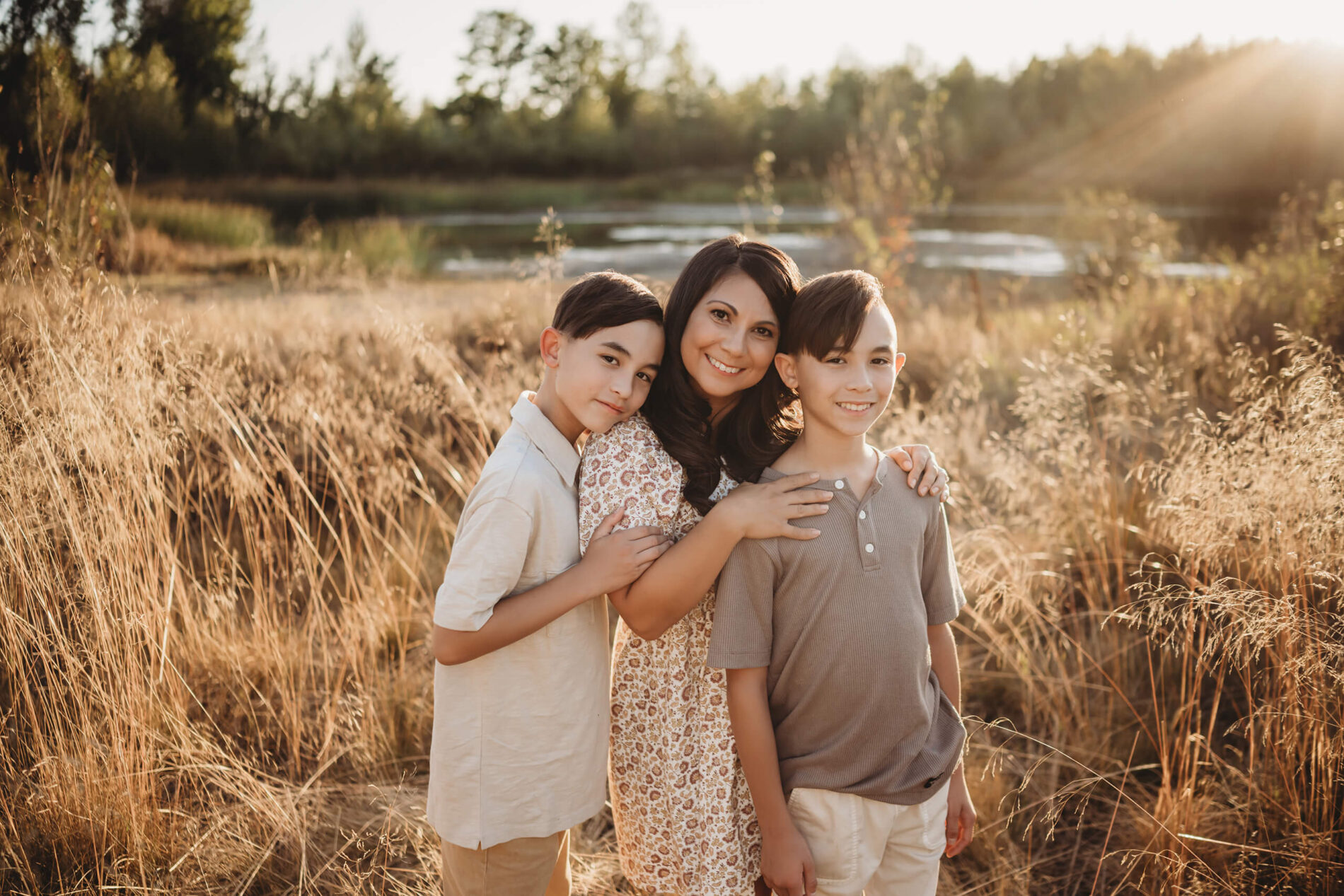 Lifestyle family photography of a mom with her two sons in a field during sunset with a pond in the background