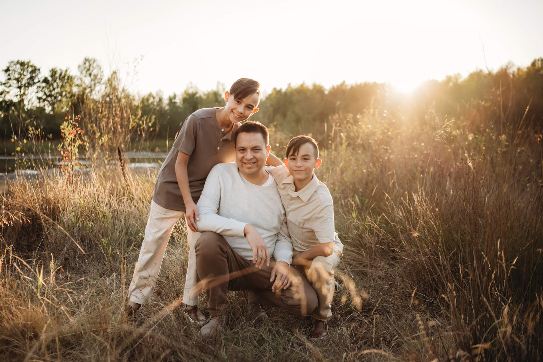 Lifestyle family photography of a dad with this two sons in a field during sunset