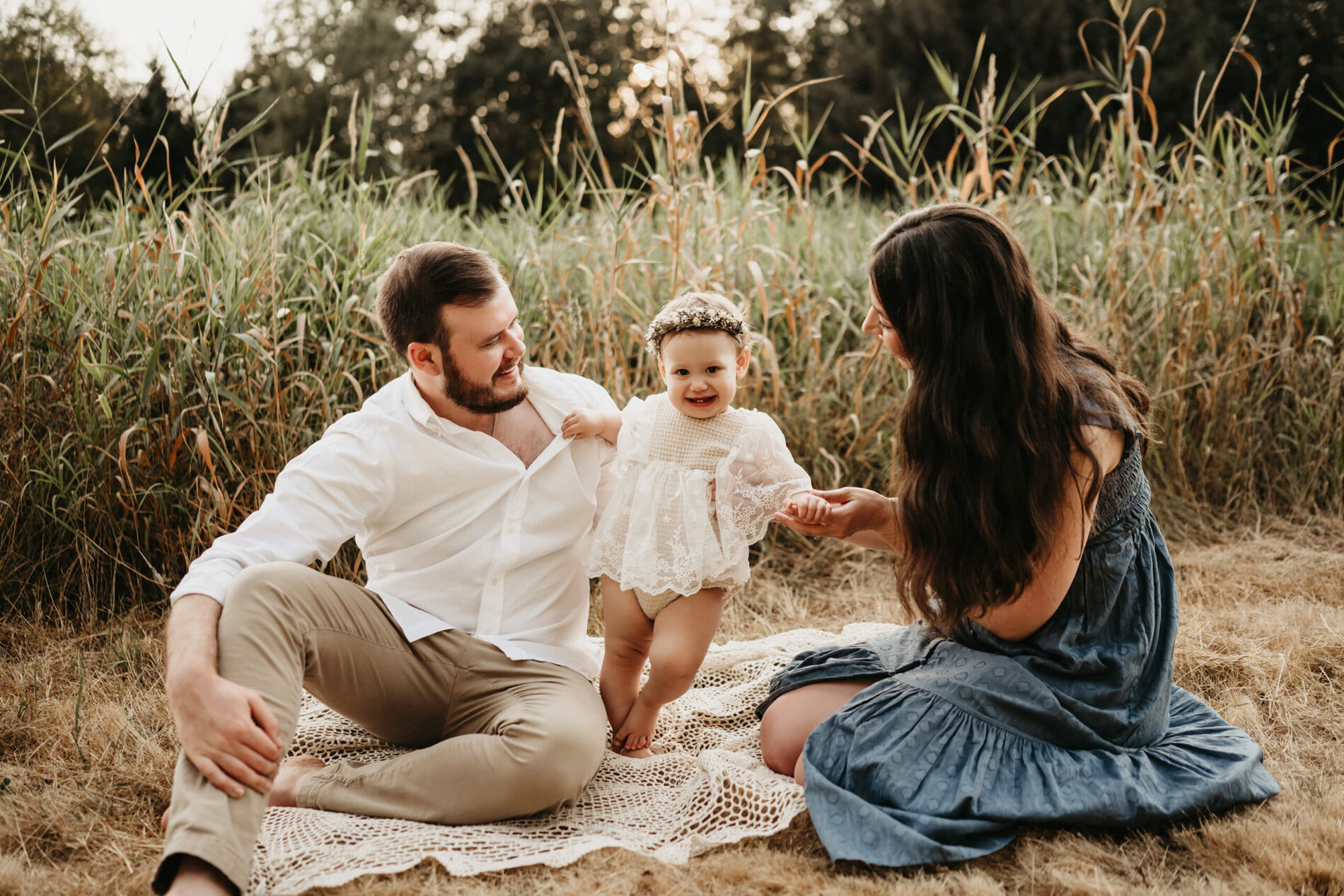 Family lifestyle photo session of mom and dad playing with their toddler daughter, sitting in a field of tall grass