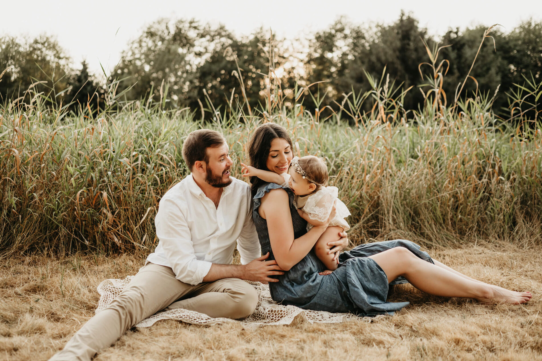 Family lifestyle photo session of mom and dad playing with their toddler daughter, sitting in a field of tall grass