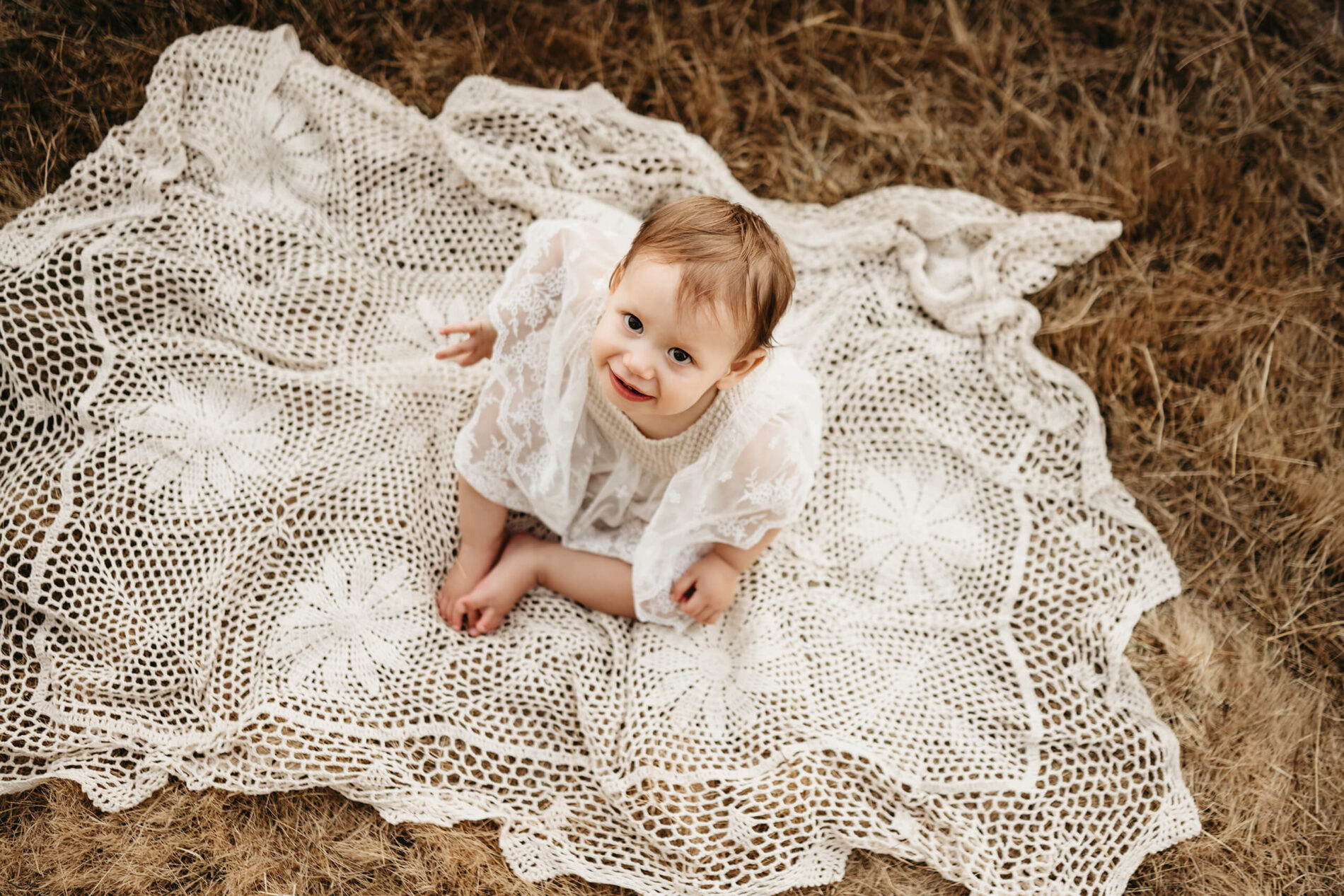 A happy toddler girl sitting on a blanket in a field