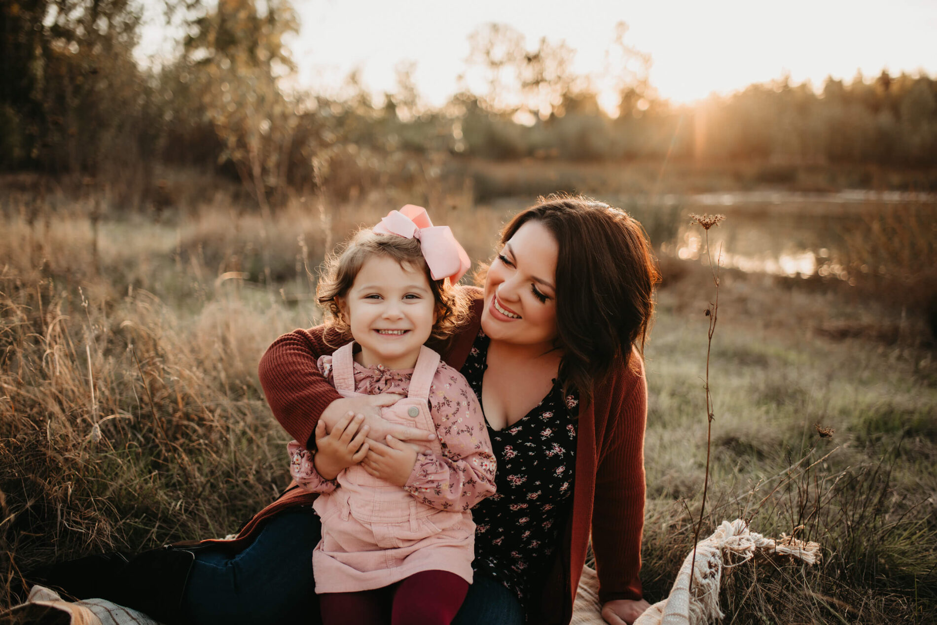 A family photo shoot in Redmond, WA with mom and daughter sitting in a field, both smiling