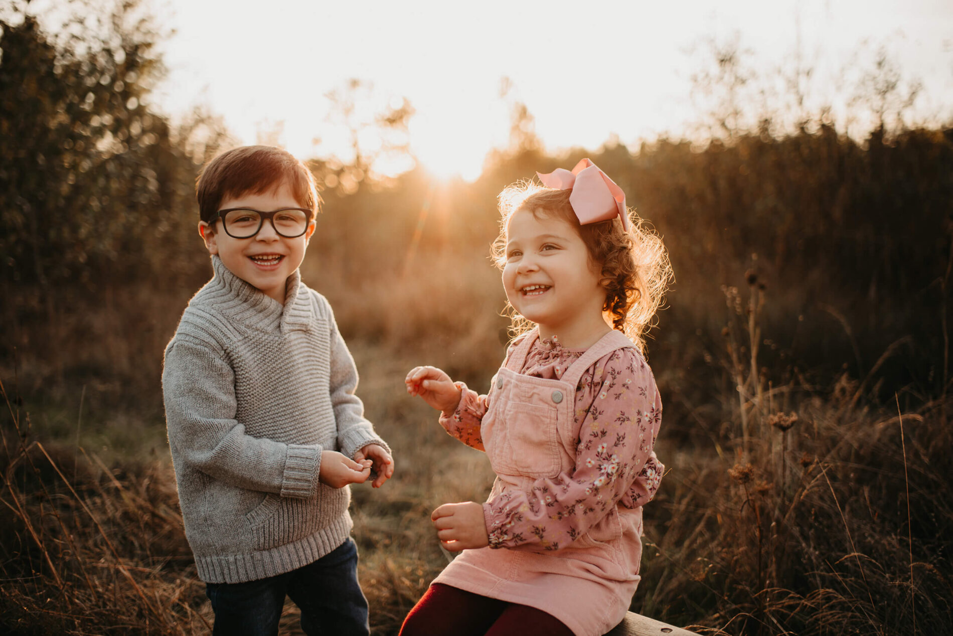 Family photo shoot of a brother and sister smiling at a field during sunset