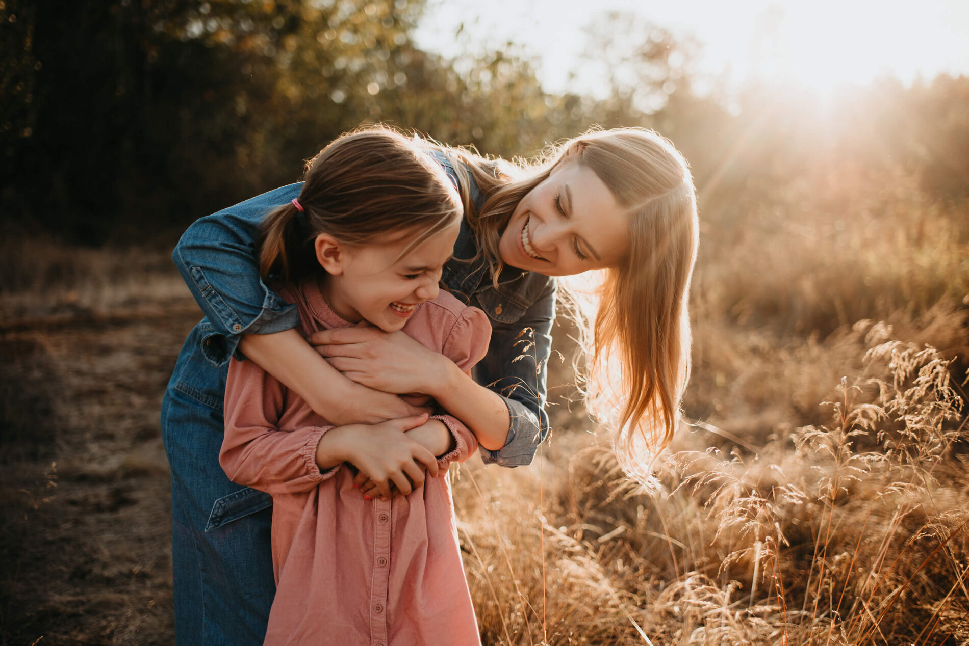 Family lifestyle portrait of mom hugging her daughter from behind, both smiling and having fun