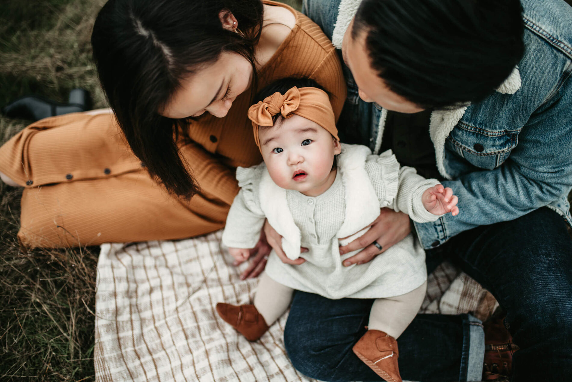 Family lifestyle photo session of two young parents sitting in a field with their toddler daughter