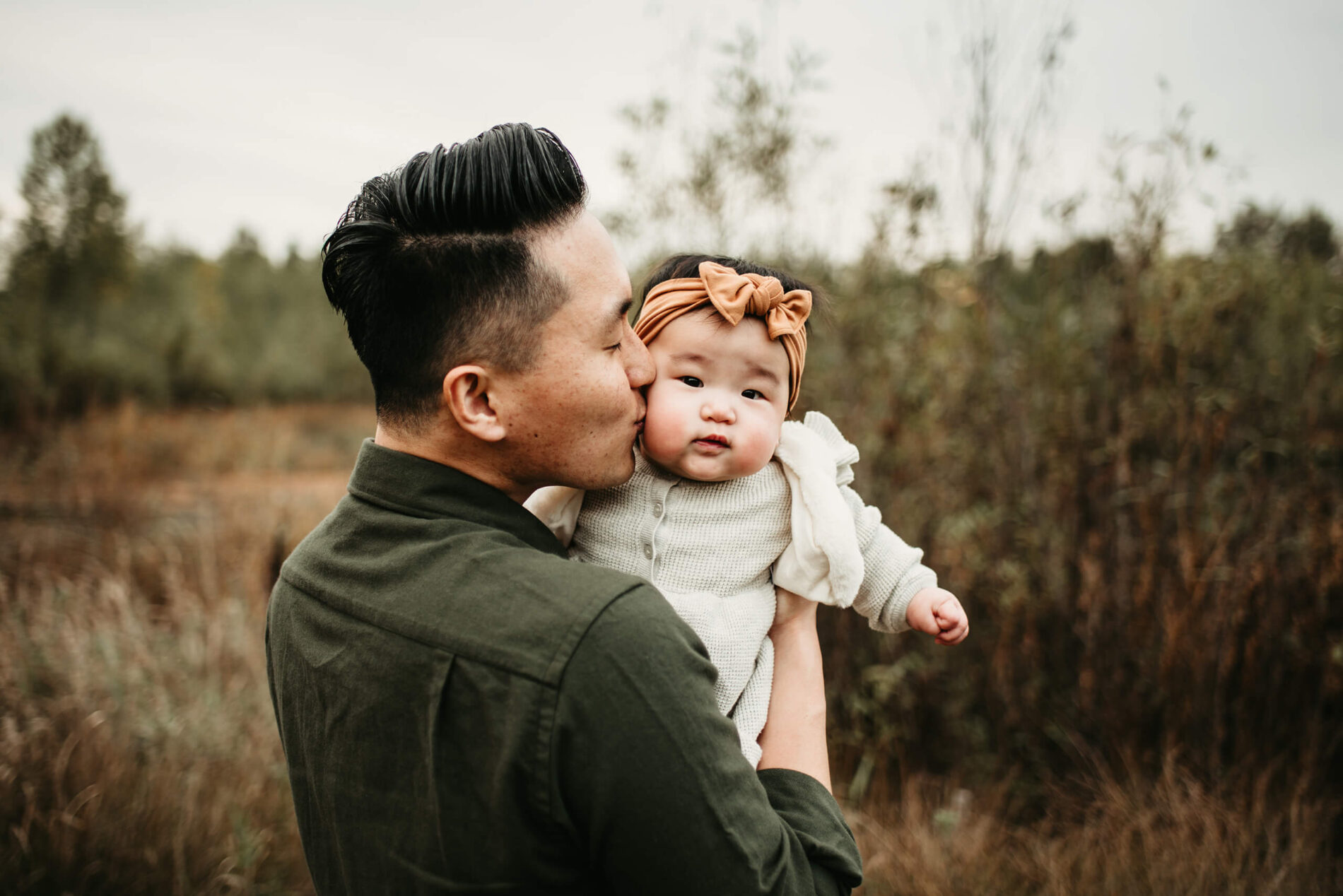 Family lifestyle portrait of a dad kissing with his toddler daughter in natural scenic setting