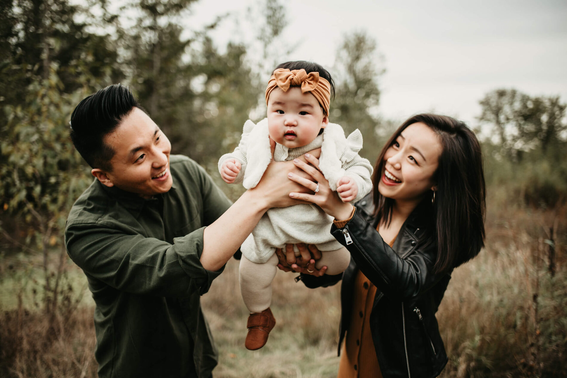 Family lifestyle portrait of two happy young parents playing with their toddler daughter in a natural scenic setting