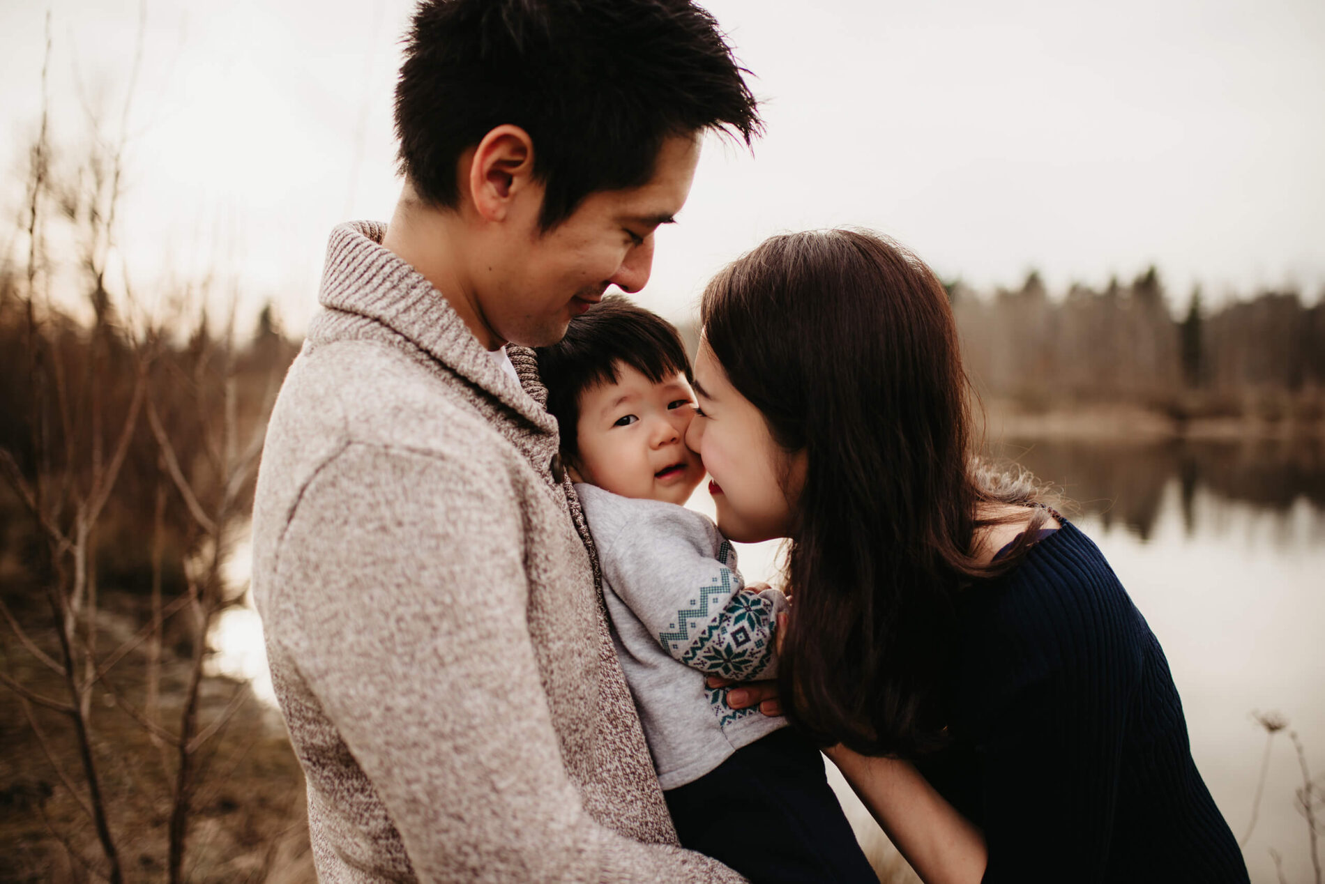 Family lifestyle photo session of two parents playing with their toddler son in a natural setting with a pond in the background