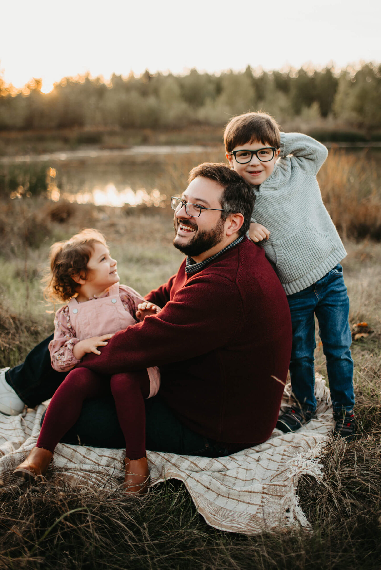 A family photo shoot of dad with two kids in a field sitting on a blanket