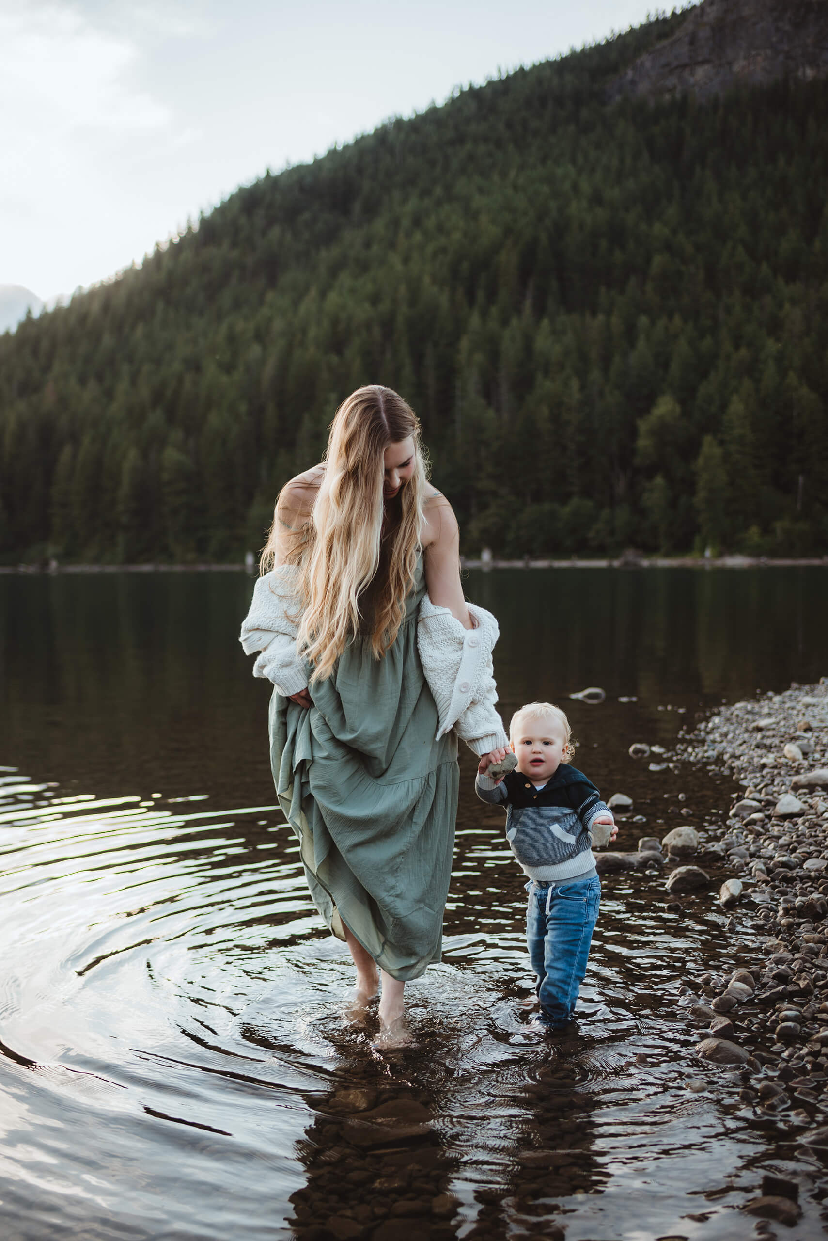 Smiling mom and son playing on the beach of a lake with mountain views in the background