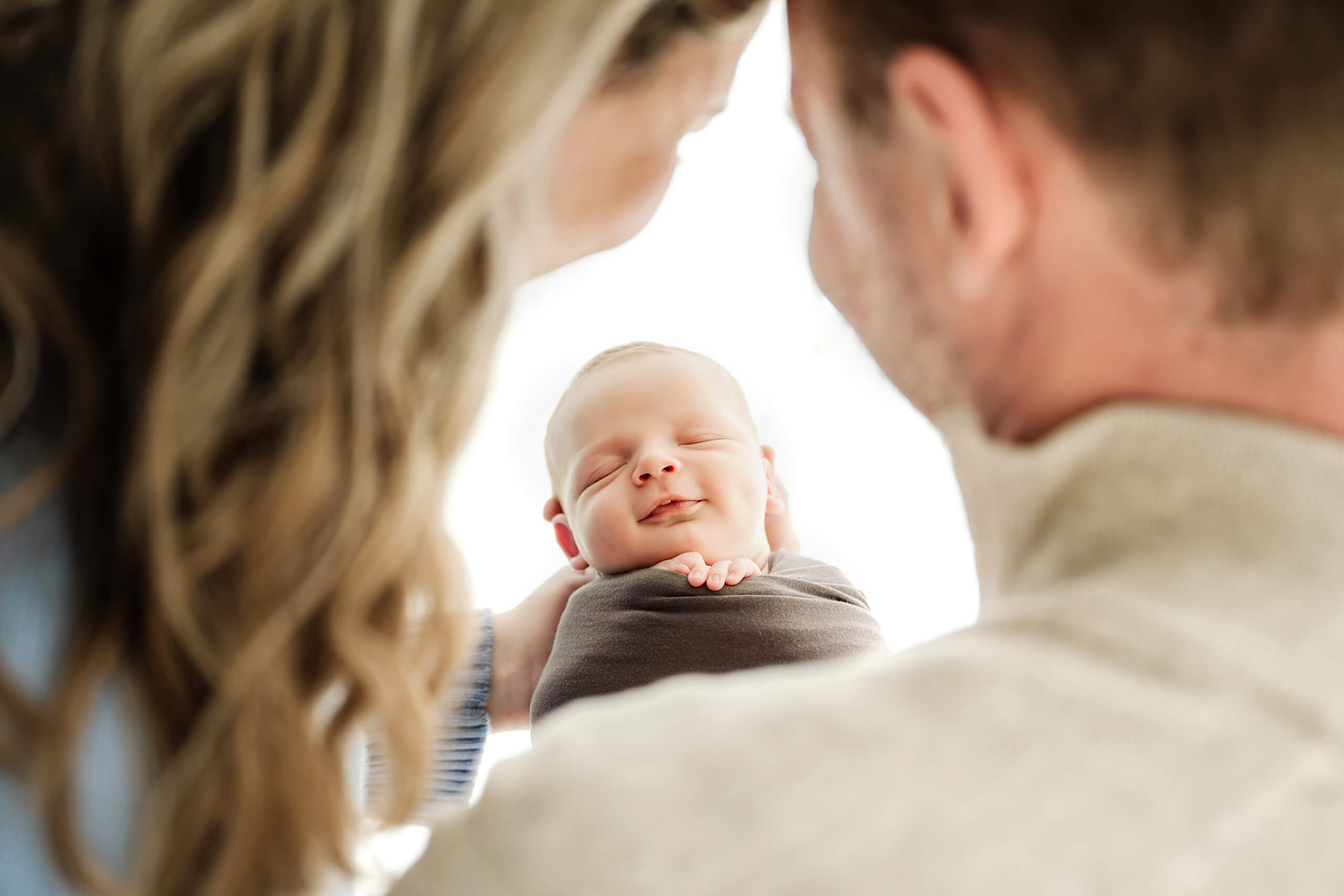 Parents frame their swaddled newborn in a cozy Seattle studio newborn family photoshoot, baby smiling softly in their arms