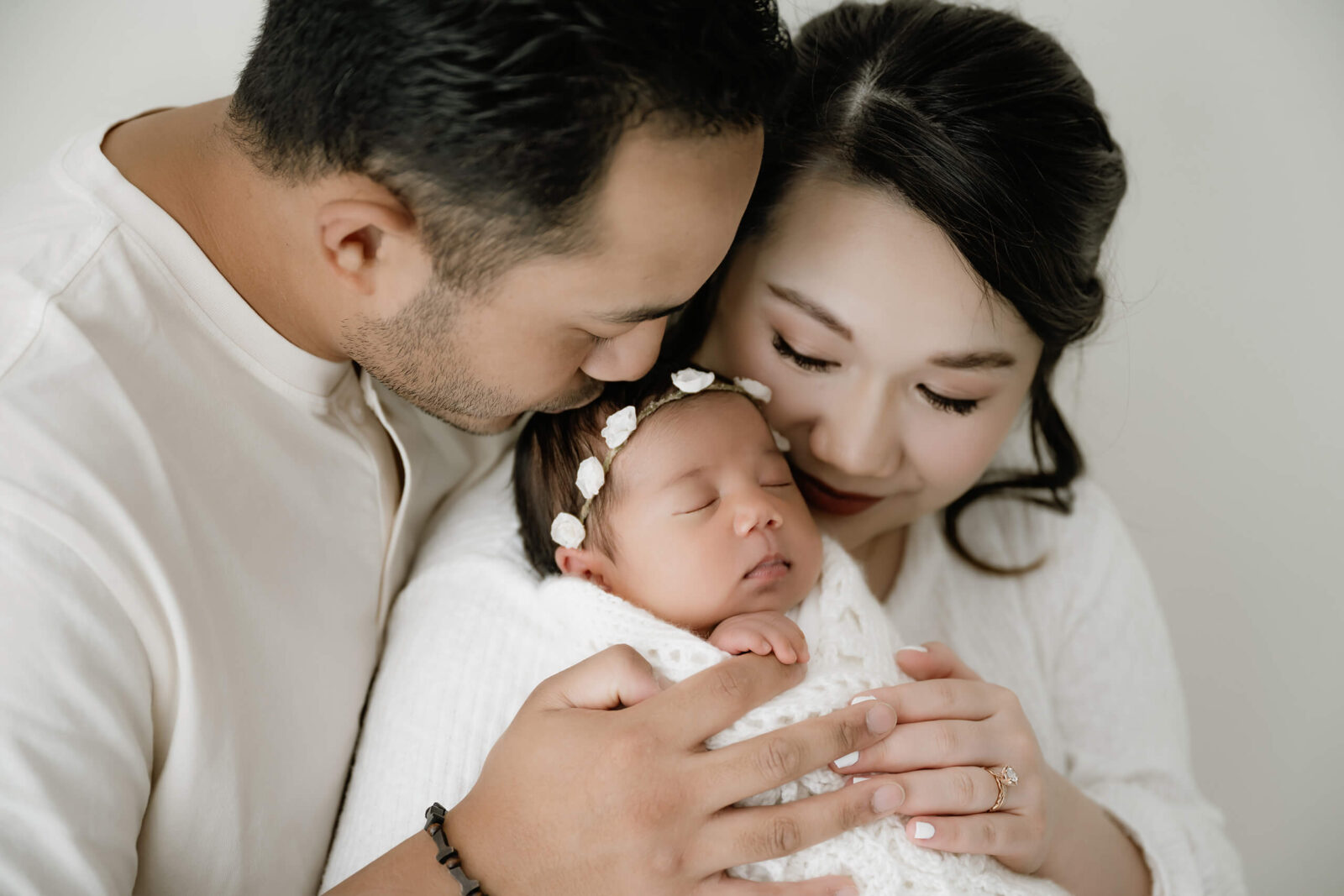 Parents hold their sleeping newborn in a white wrap during a Seattle family newborn photography session, baby wearing a delicate floral headband