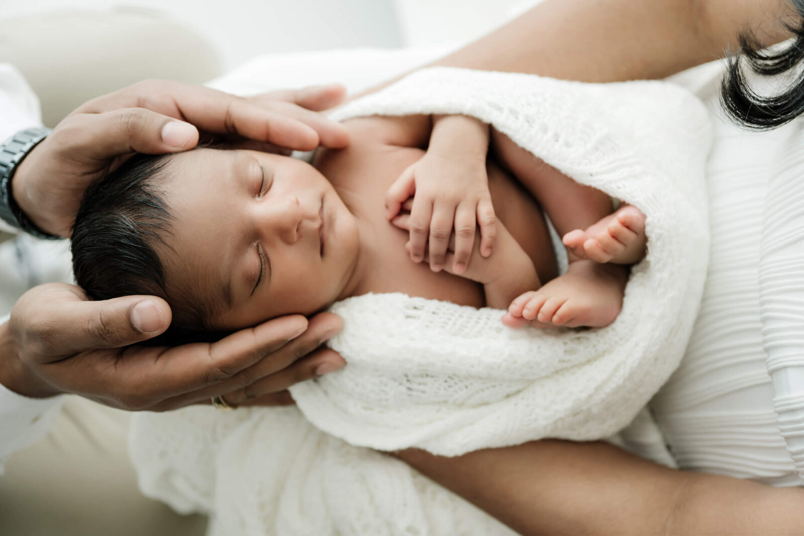 Sleeping newborn curled in a parent’s arms with a soft white wrap during a Seattle family newborn photoshoot, hands gently supporting baby’s head