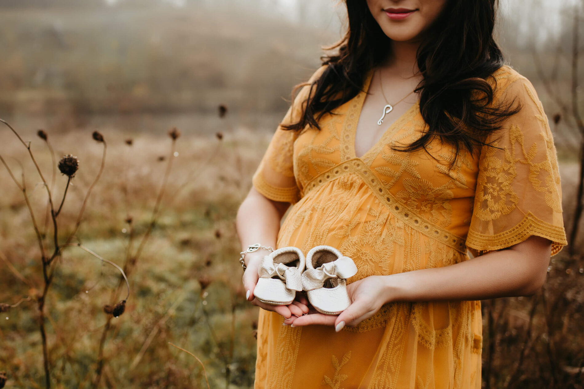 A woman holding small shoes during a winter maternity photo shoot