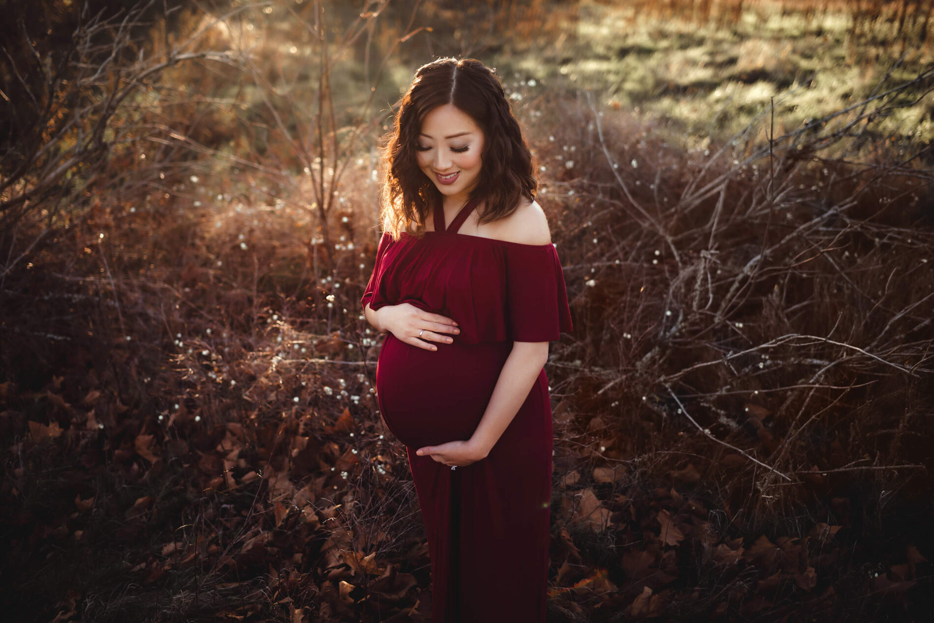 Smiling woman posing during outdoor winter maternity photo shoot at sunset