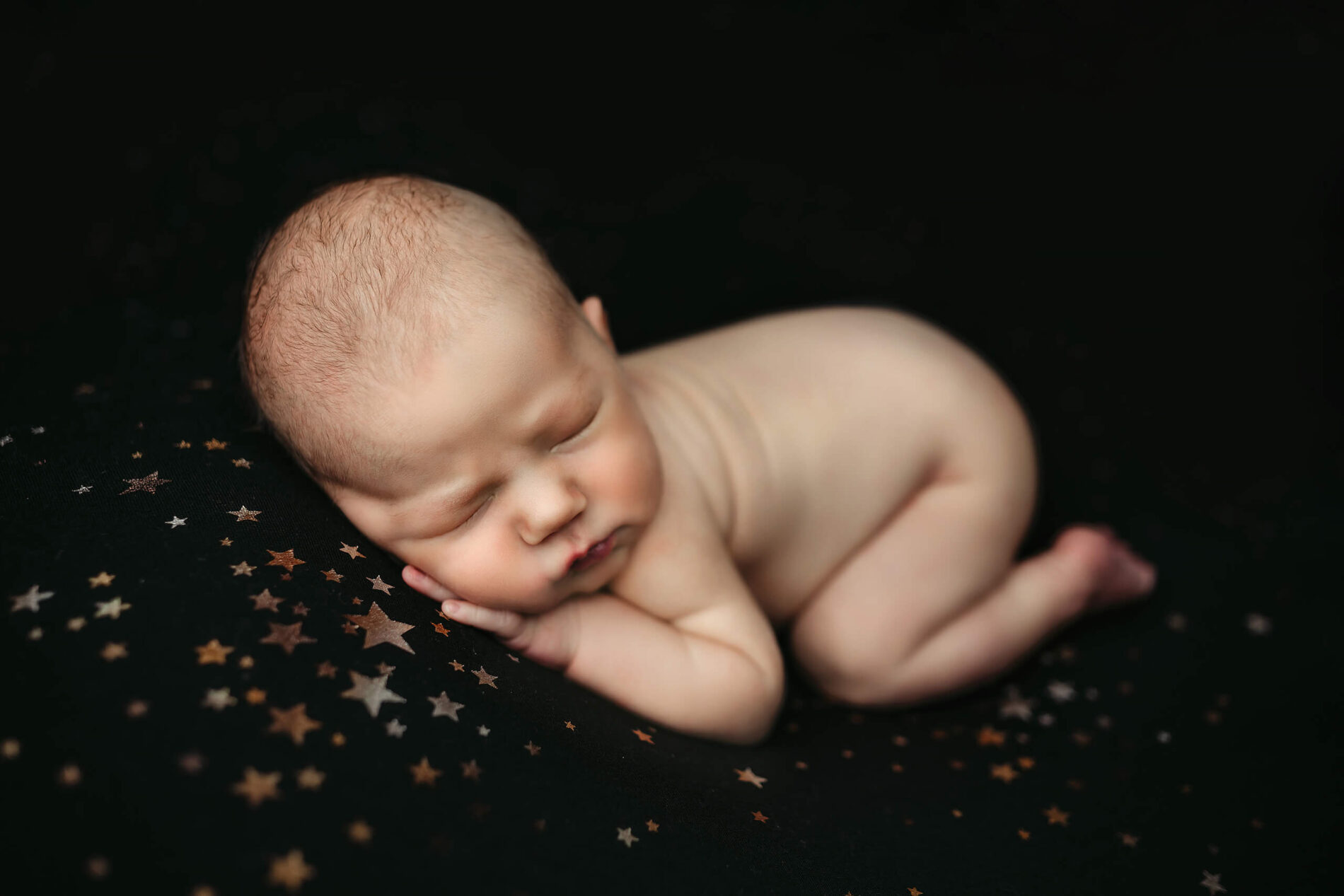 Baby boy sleeping on his tummy with hands under his cheek during newborn photo shoot in Bellevue area
