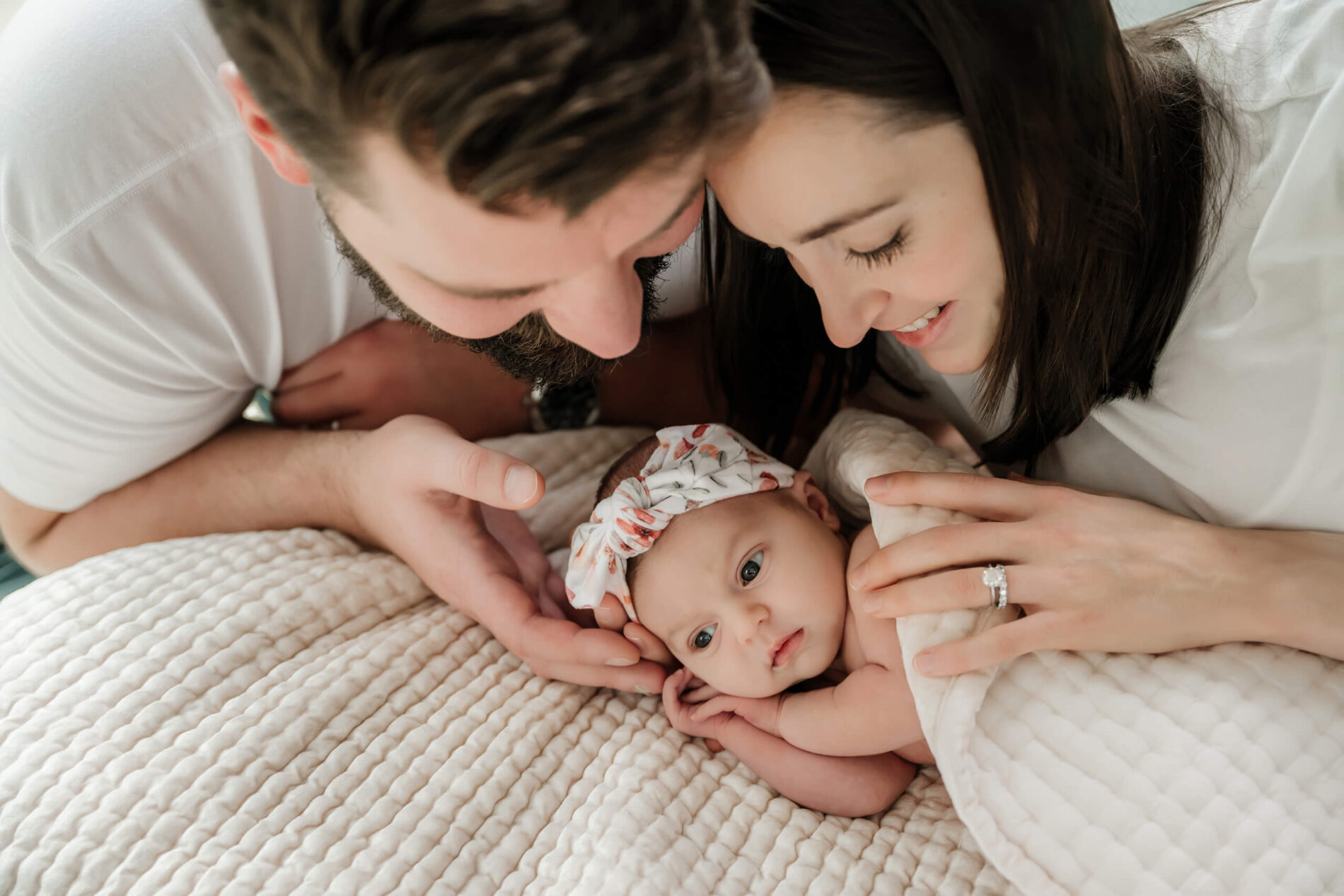 Family lying on the bed with their daughter during at home newborn photo shoot