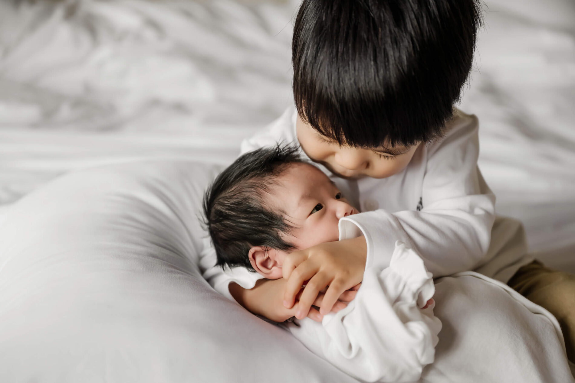 Toddler hugging baby brother on a bed during newborn photo shoot in Seattle