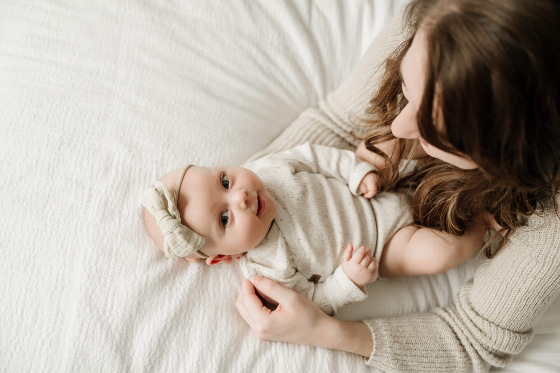 Newborn photo shoot at home of mom and her happy baby girl cuddling on the bed