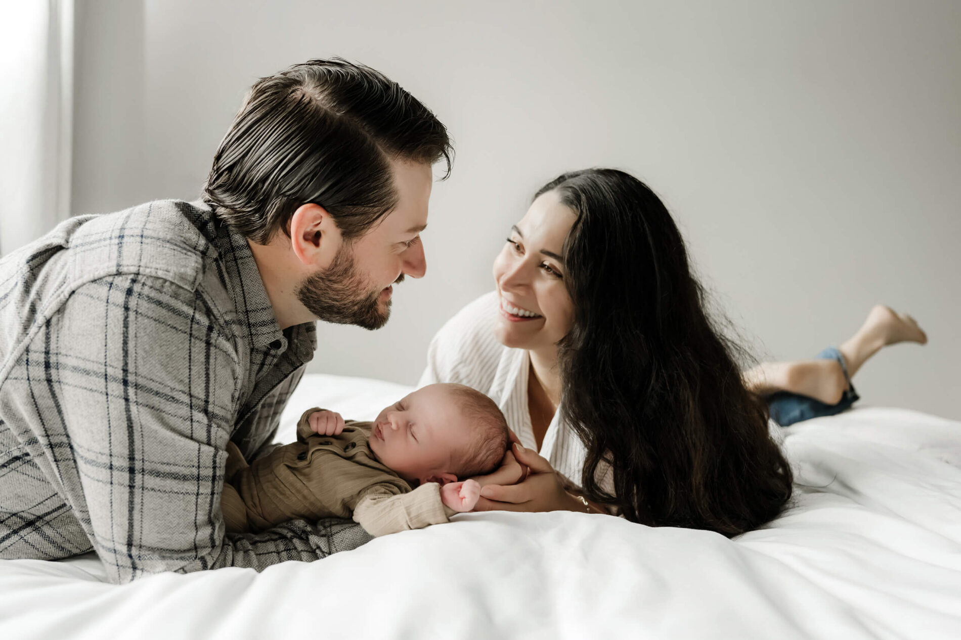 Happy parents looking at each other with their baby son lying on a bed during newborn photo shoot at home