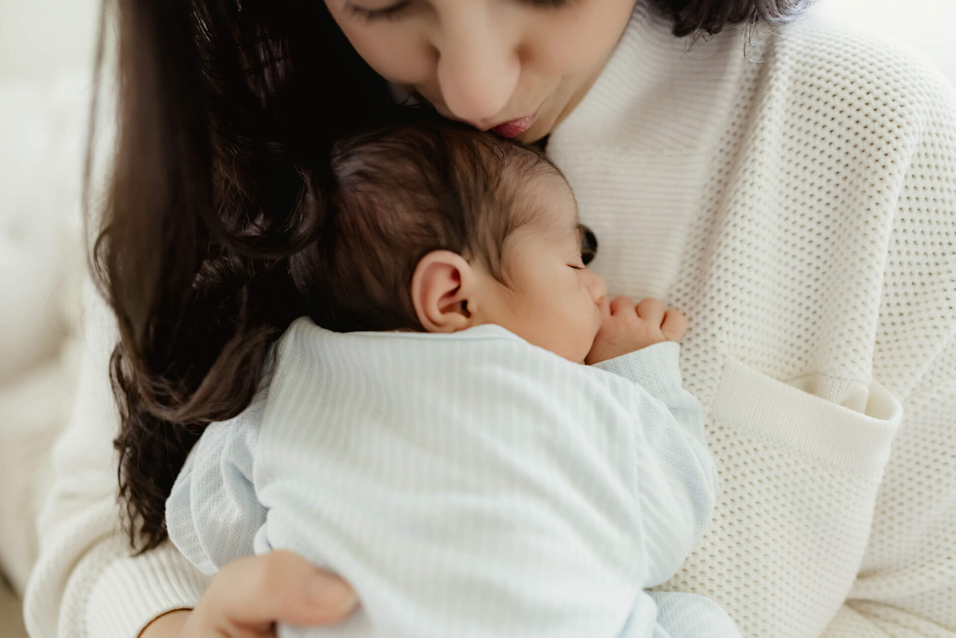 Moment during newborn photo shoot, mom lovingly kissing baby boy's head