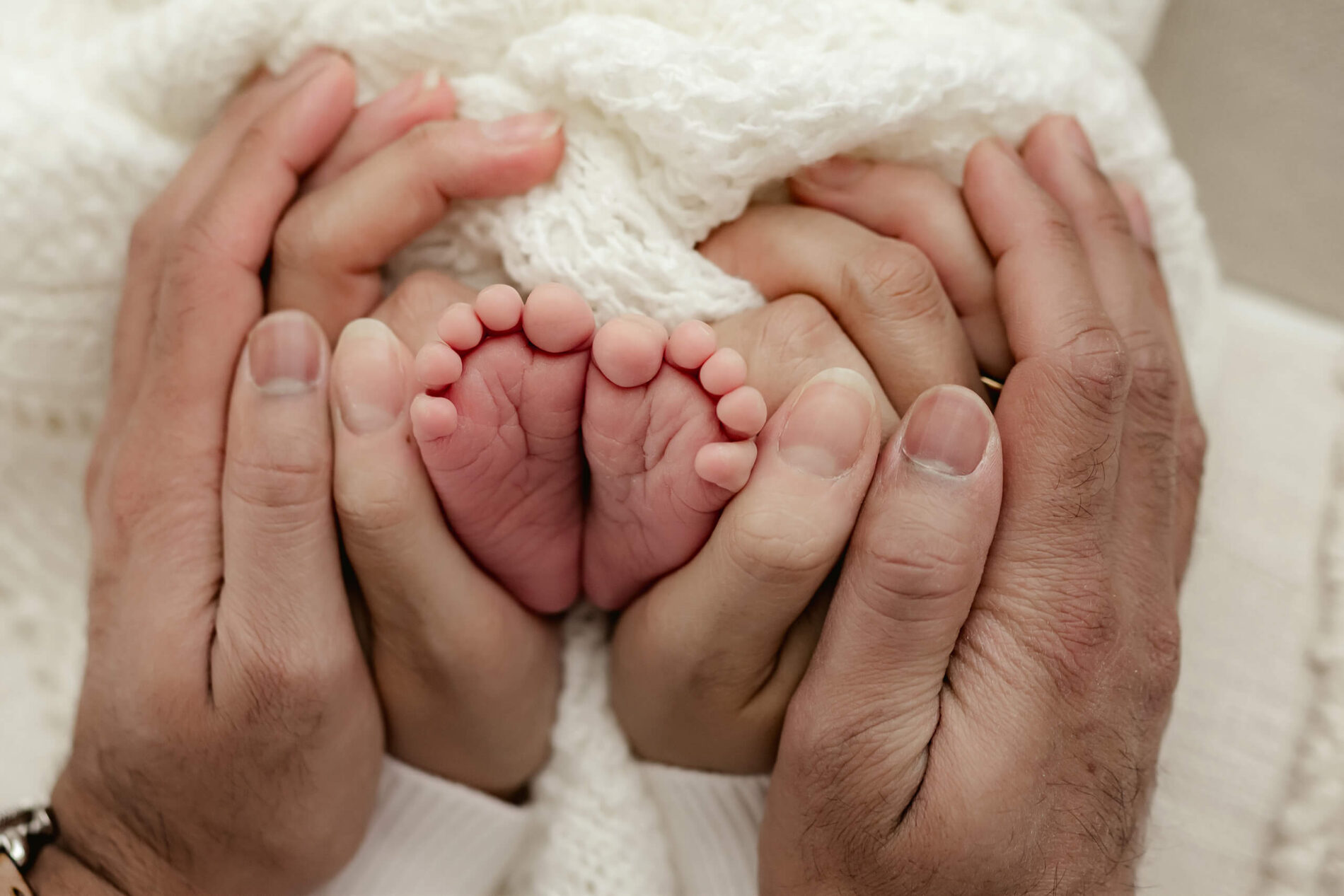 Newborn photography in Seattle, focus on parent's hands wrapped around baby's feet