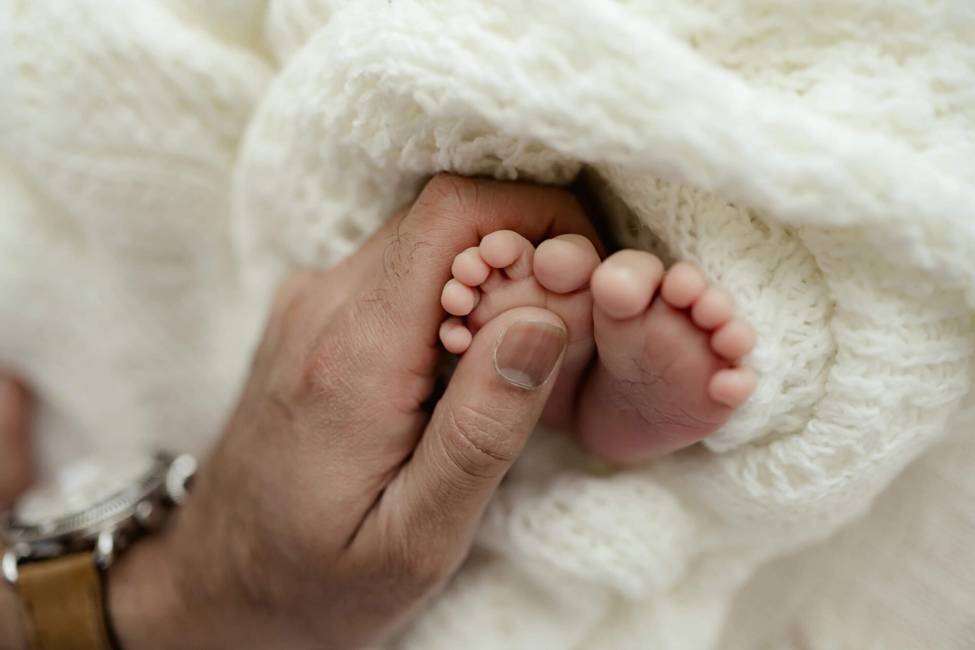 Newborn photography, close-up of dad's hands gently touching baby's feet