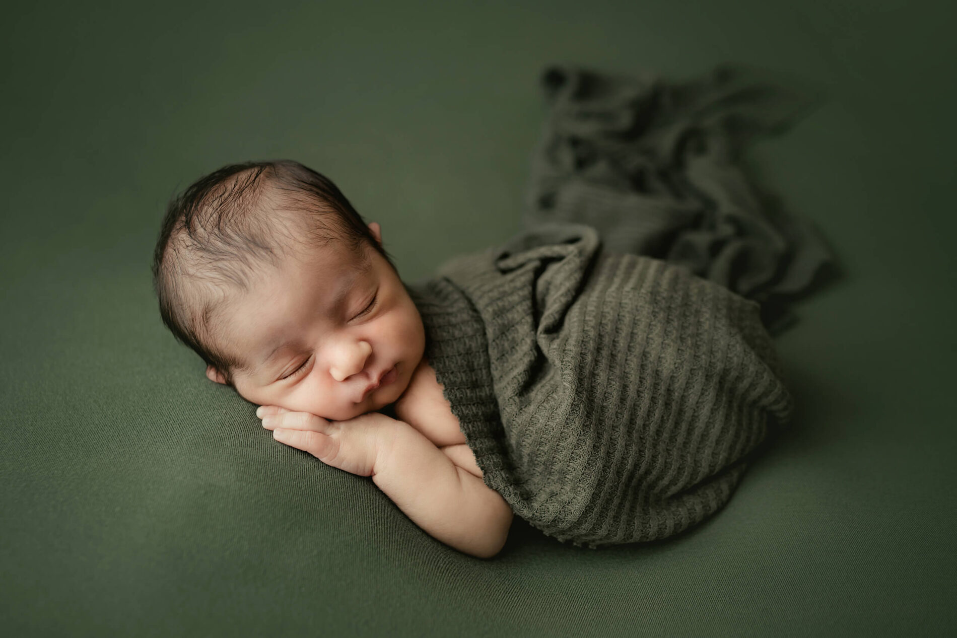 Newborn photography in a Seattle studio, posed baby boy sleeping covered with green blanket