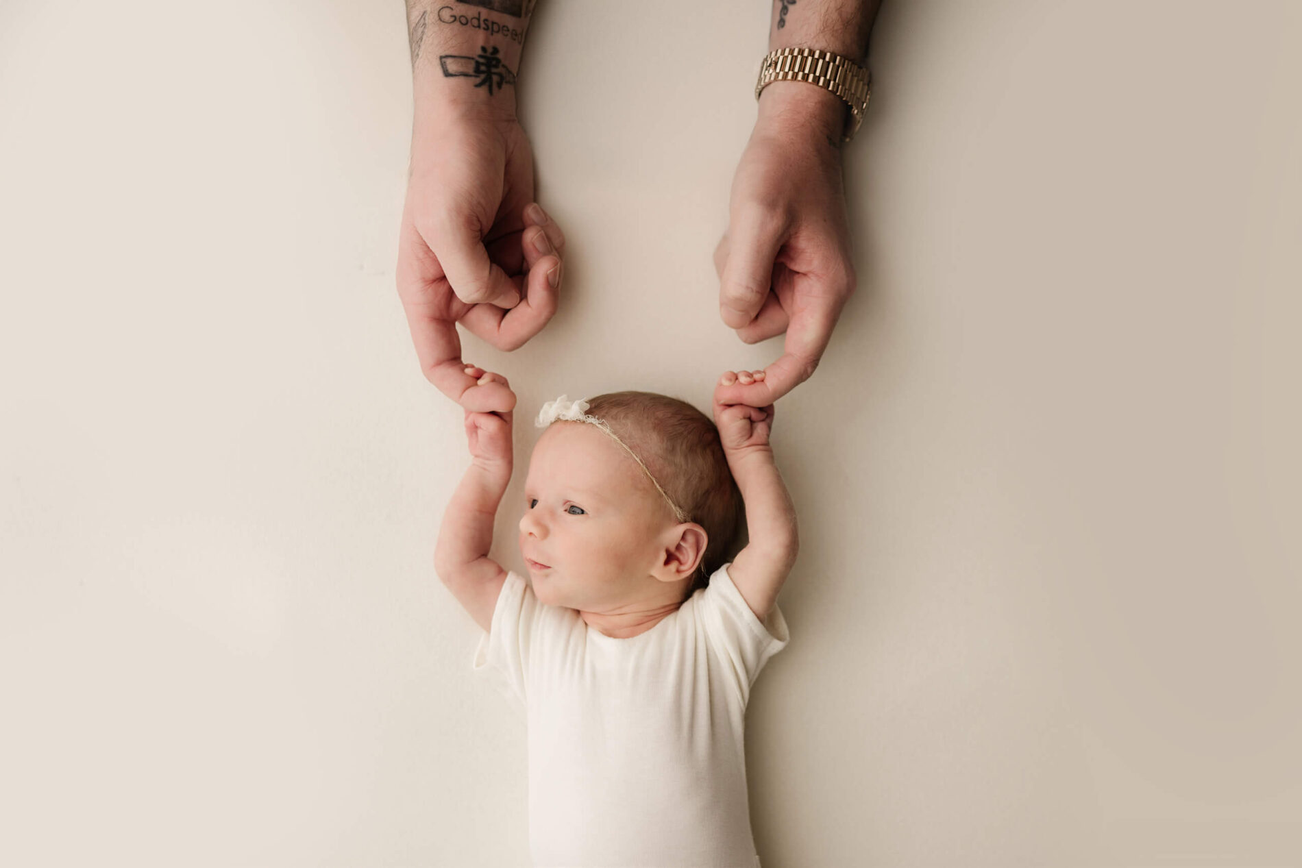 Newborn photography, baby girl lying on her back with her hands above her head, squeezing dad's fingers