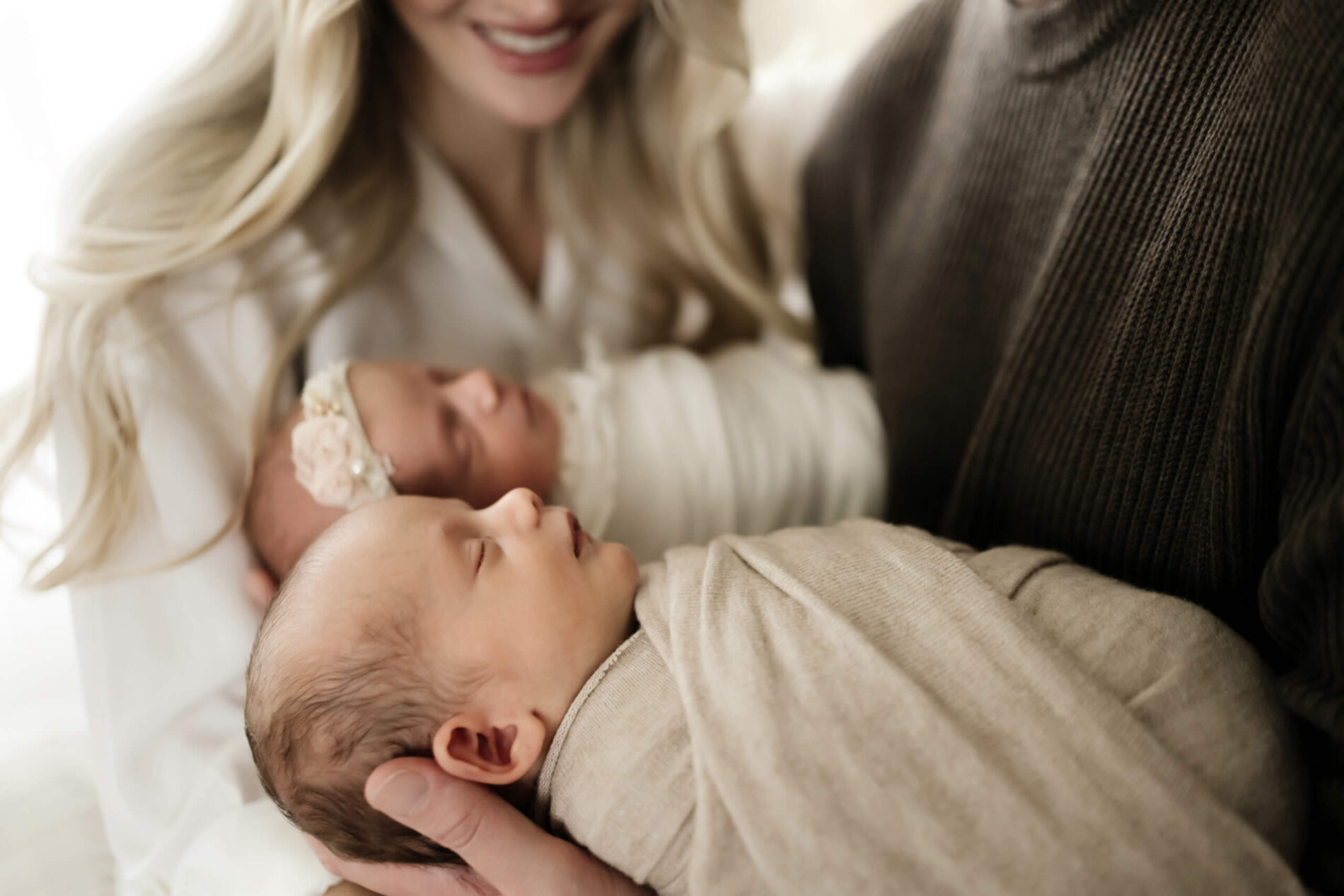 Newborn twin photography with parents, dad holding son and daughter with mom standing behind them
