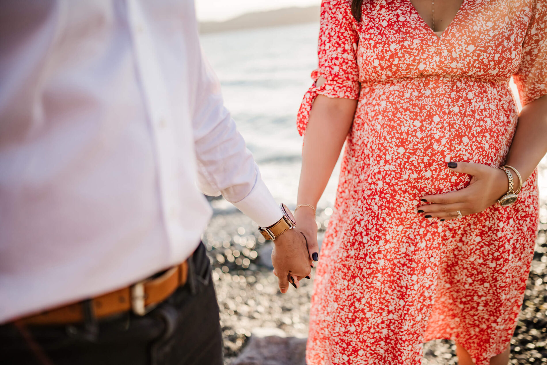 Beach maternity photography idea in Seattle, WA, young couple holding hands, focus on mom's tommy