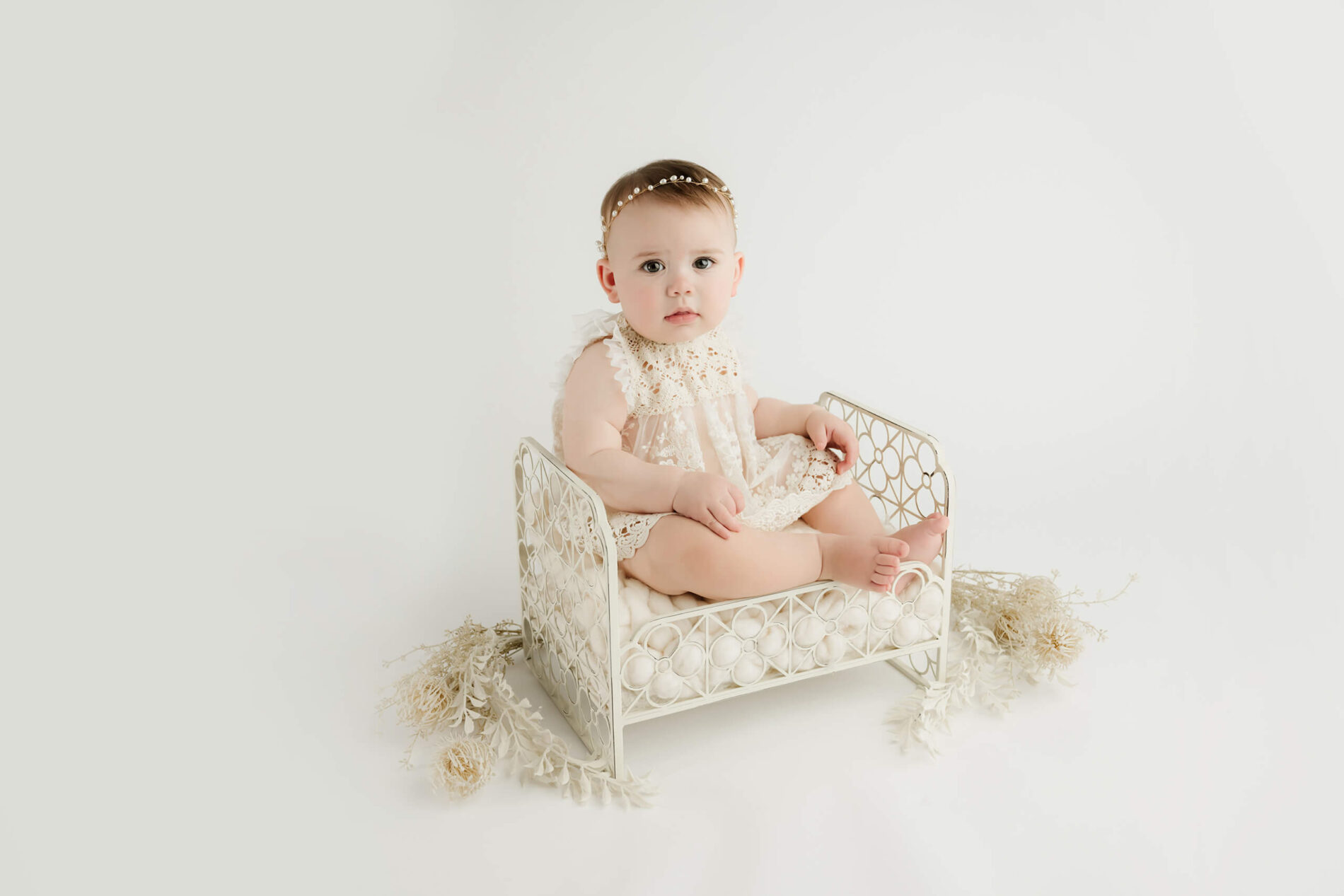 Child milestone session, toddler girl in a dress sitting in a prop bed on a white background