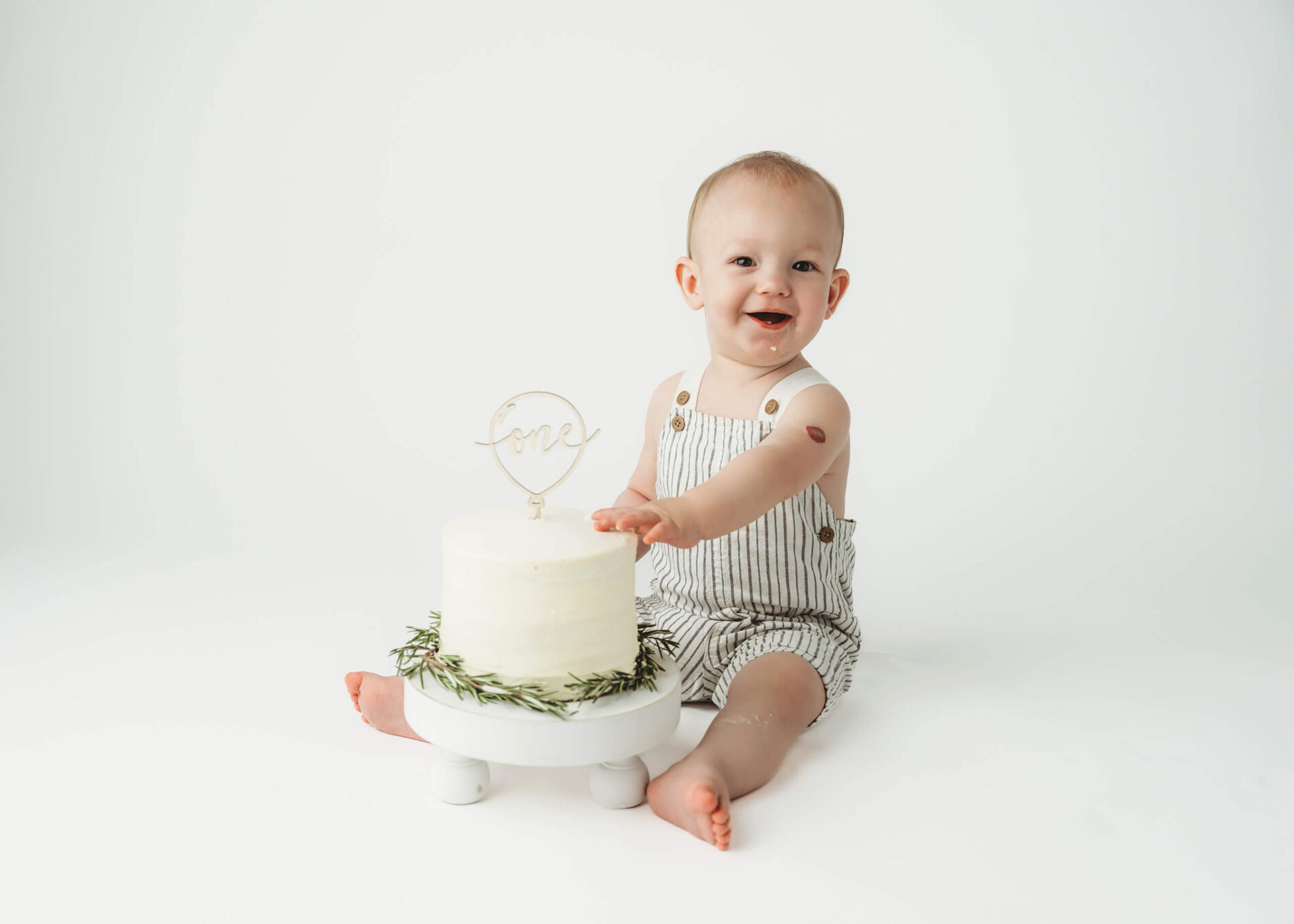 Cake smash session in Seattle, one year old toddler boy sitting on a floor smiling, toughing a white cake