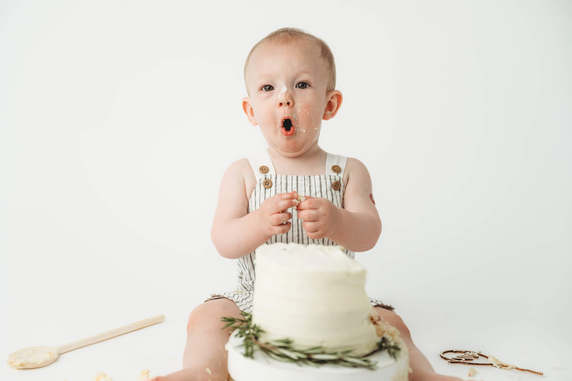 Cake smash milestone photo shoot, one year old boy looking surprised after trying some cake