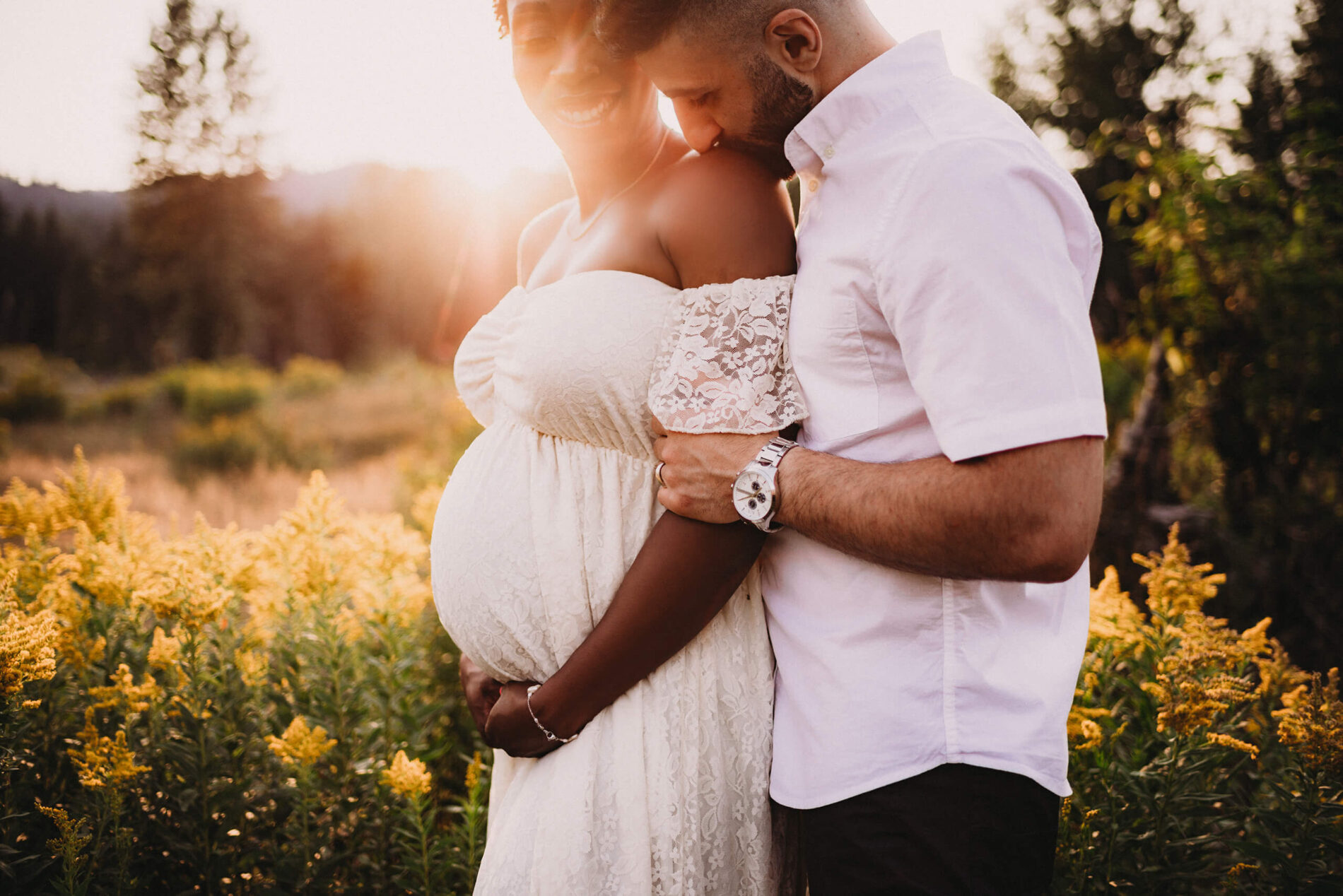 Maternity photography in the Cascades, couple in a field of wild flowers with husband gently kissing his wife on her shoulder