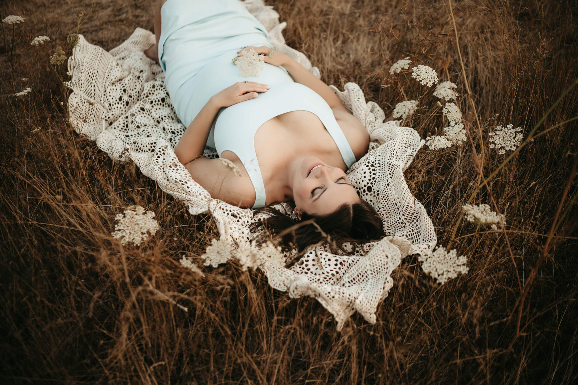 Smling maternity photography idea, pregnant woman lying on a blanket in a field of tall dress and wildflowers