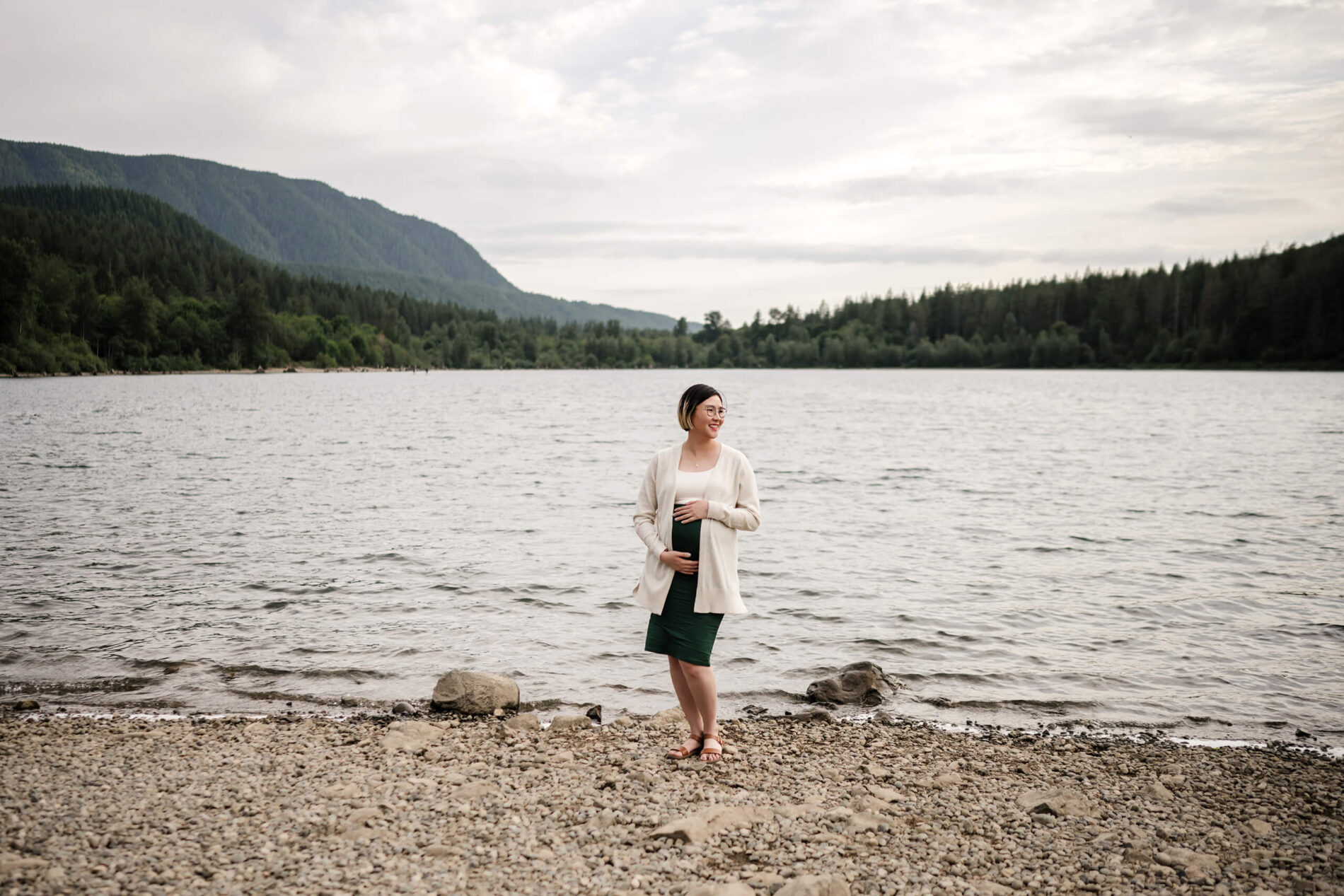 Maternity photography in the Cascades, mom standing in front of the lake with her hands on the belly, lake and mountains in the background