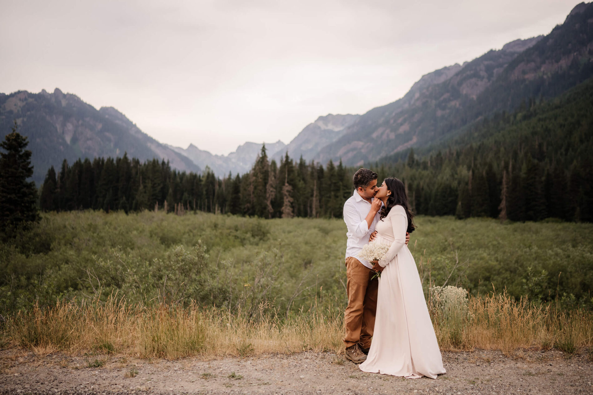 Maternity photography idea in Seattle, couple facing each other and kissing, mountains and forest behind them