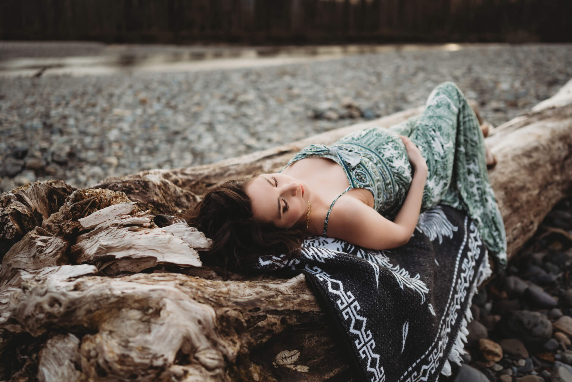Maternity photography posing idea, pregnant woman in a dress lying with eyes closed on top of a fallen tree